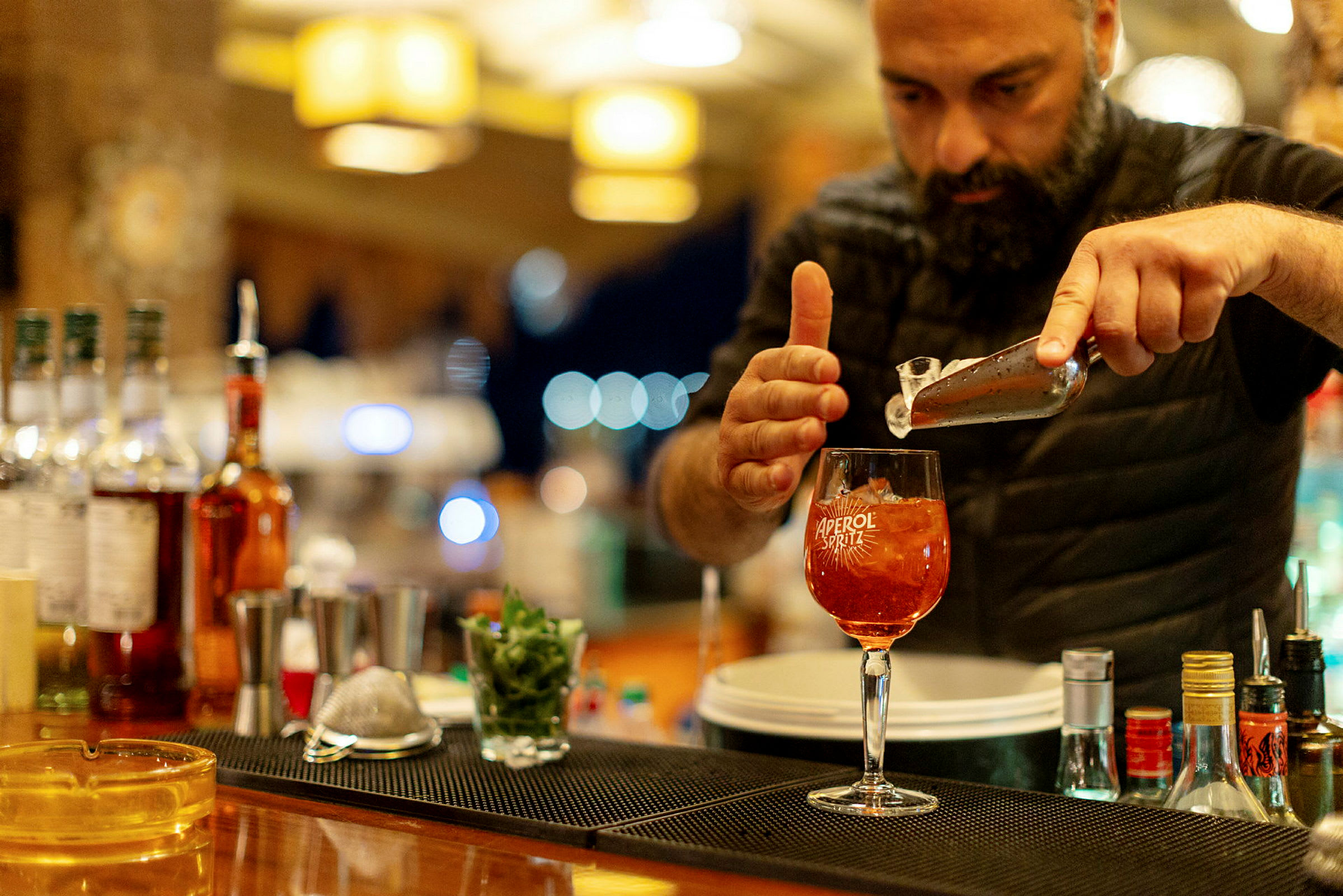 En person förbereder en Aperol Spritz vid en bardisk. (AI-genererad text)