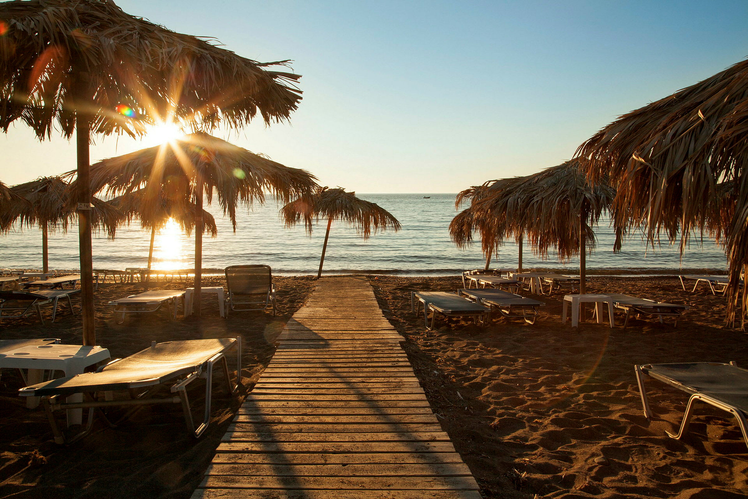 Solnedgång över en strand med solstolar och parasoll. (AI-genererad text)