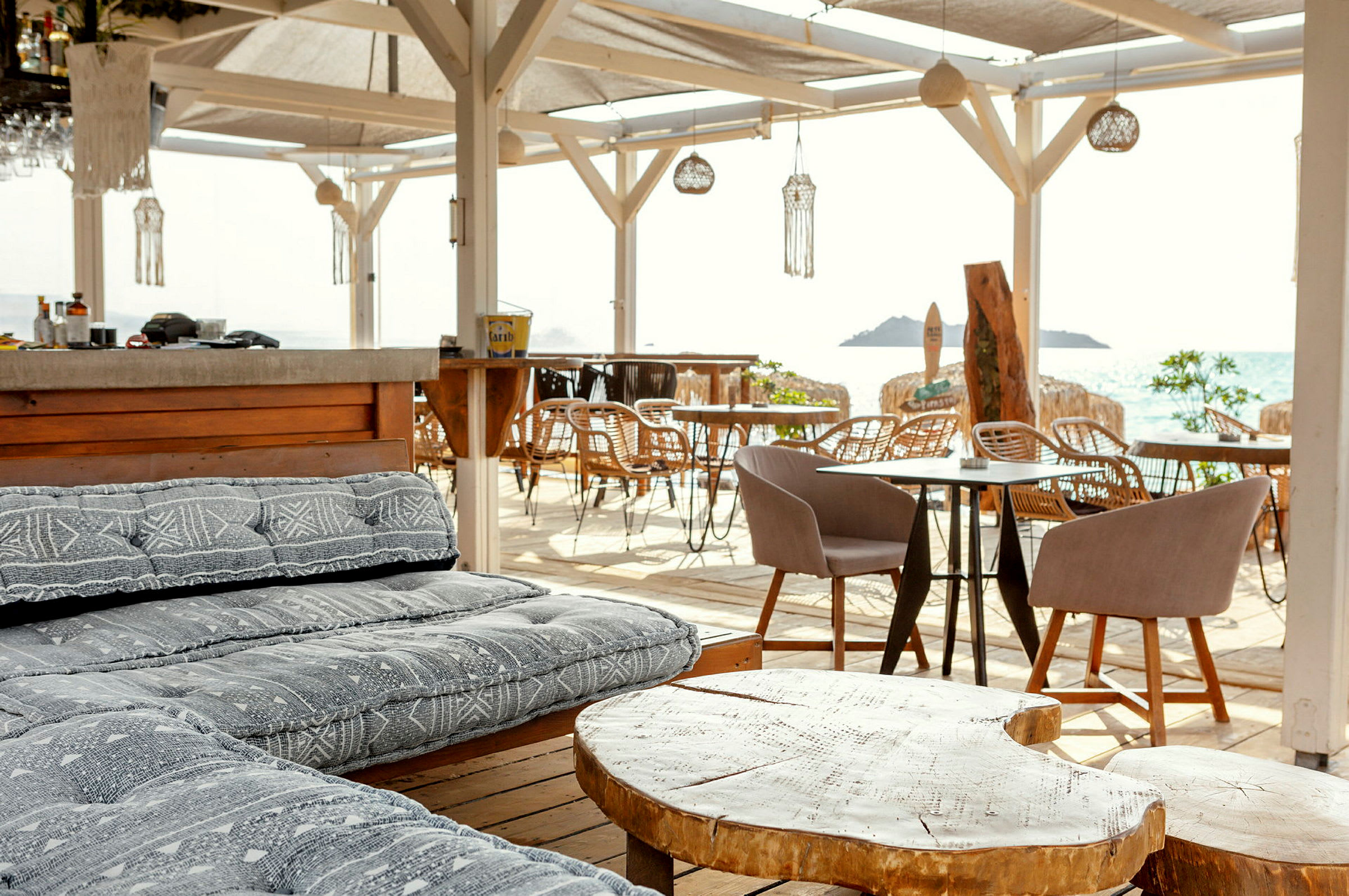 En strandbar med bekväma sittplatser, träbord, och utsikt över havet. (AI-genererad text)