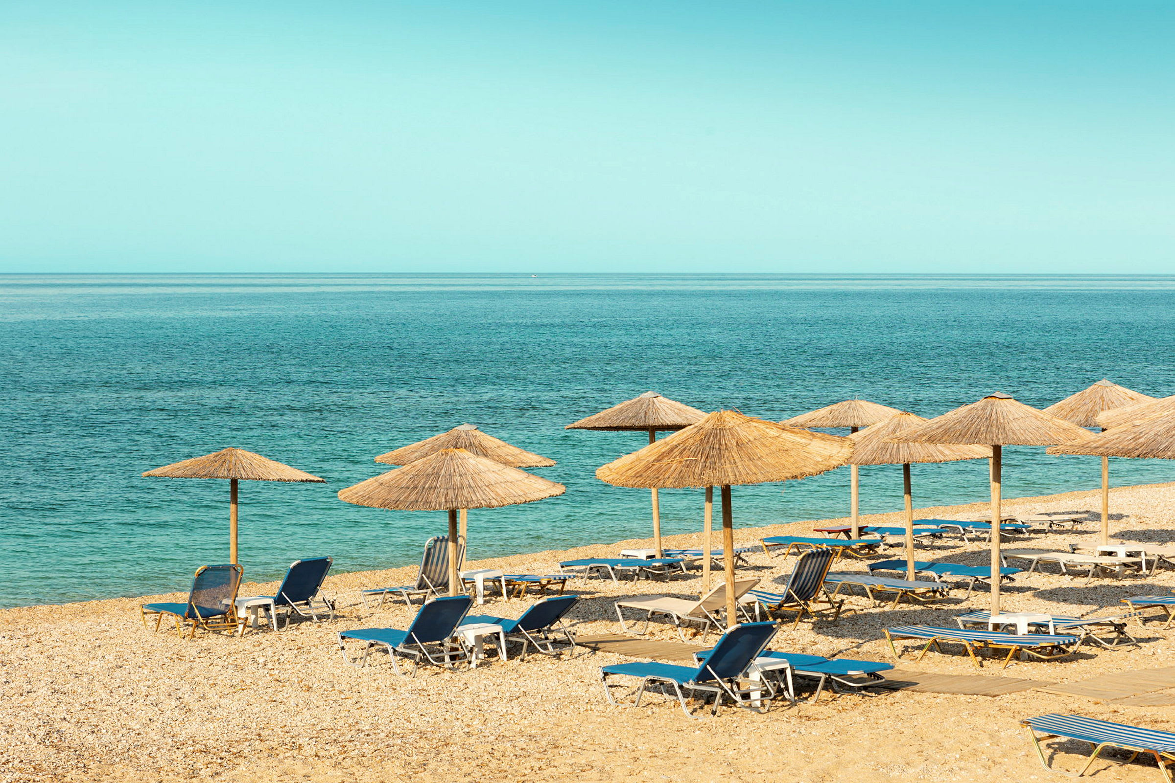 En strand med solstolar och parasoller av halm nära havet. (AI-genererad text)