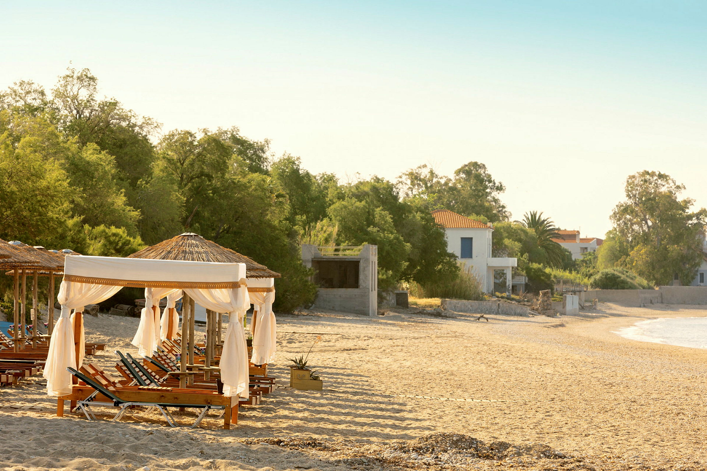 Solstolar och parasoller på en sandstrand med byggnader i bakgrunden. (AI-genererad text)