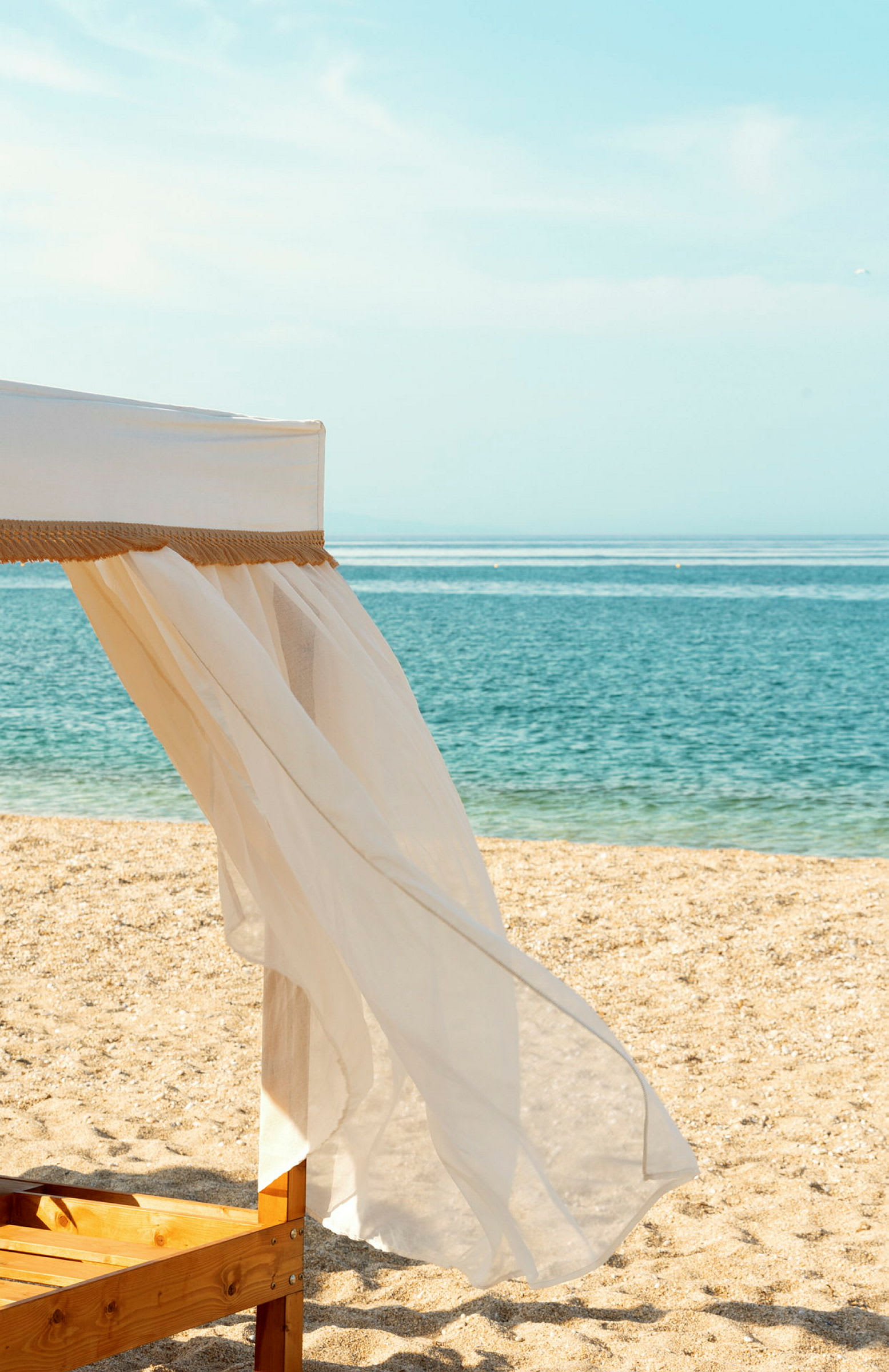 Närbild av en strand med en trästol täckt av vit tyg och havet i bakgrunden. (AI-genererad text)
