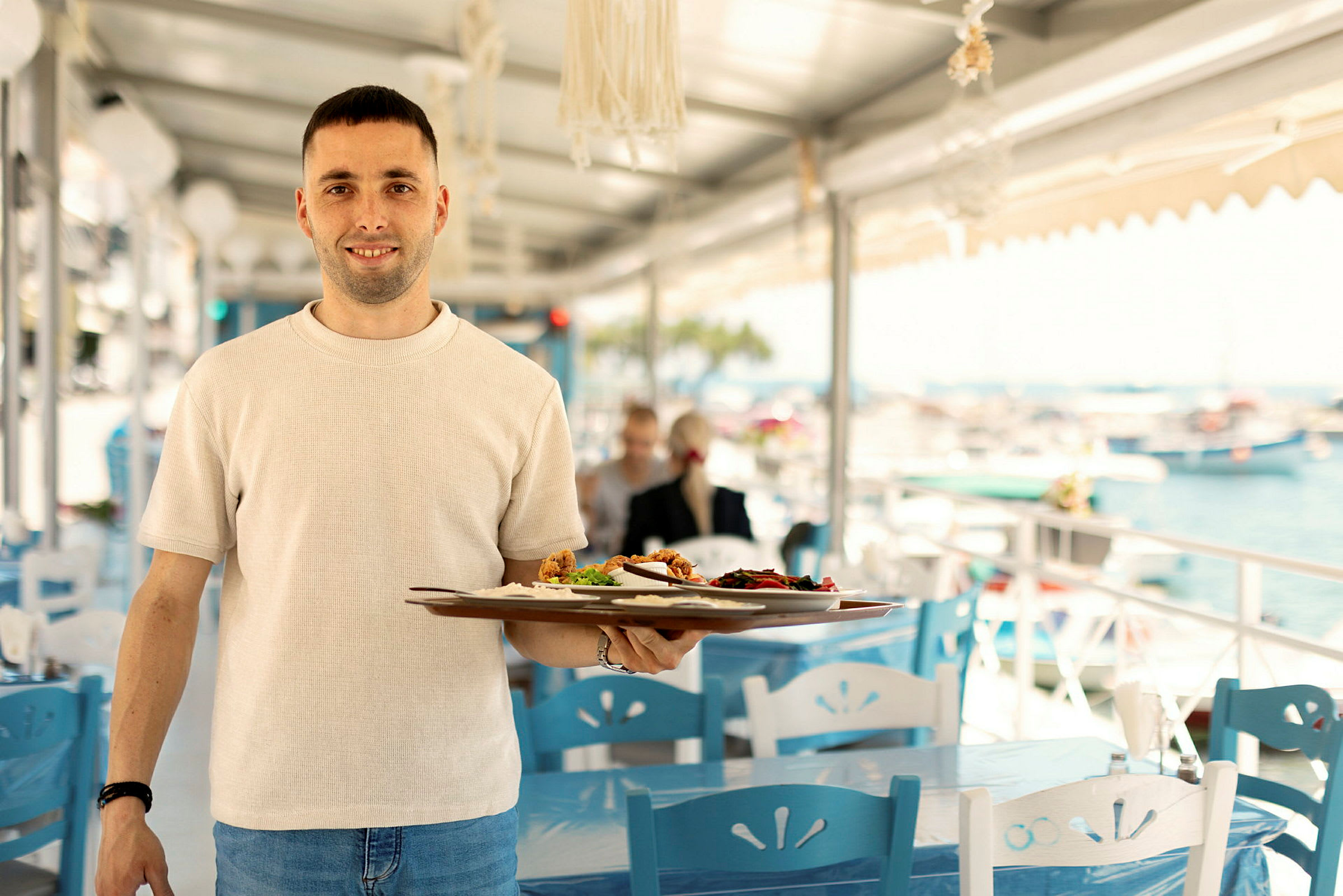 Person håller en tallrik med mat på en restaurang utomhus vid havet. (AI-genererad text)