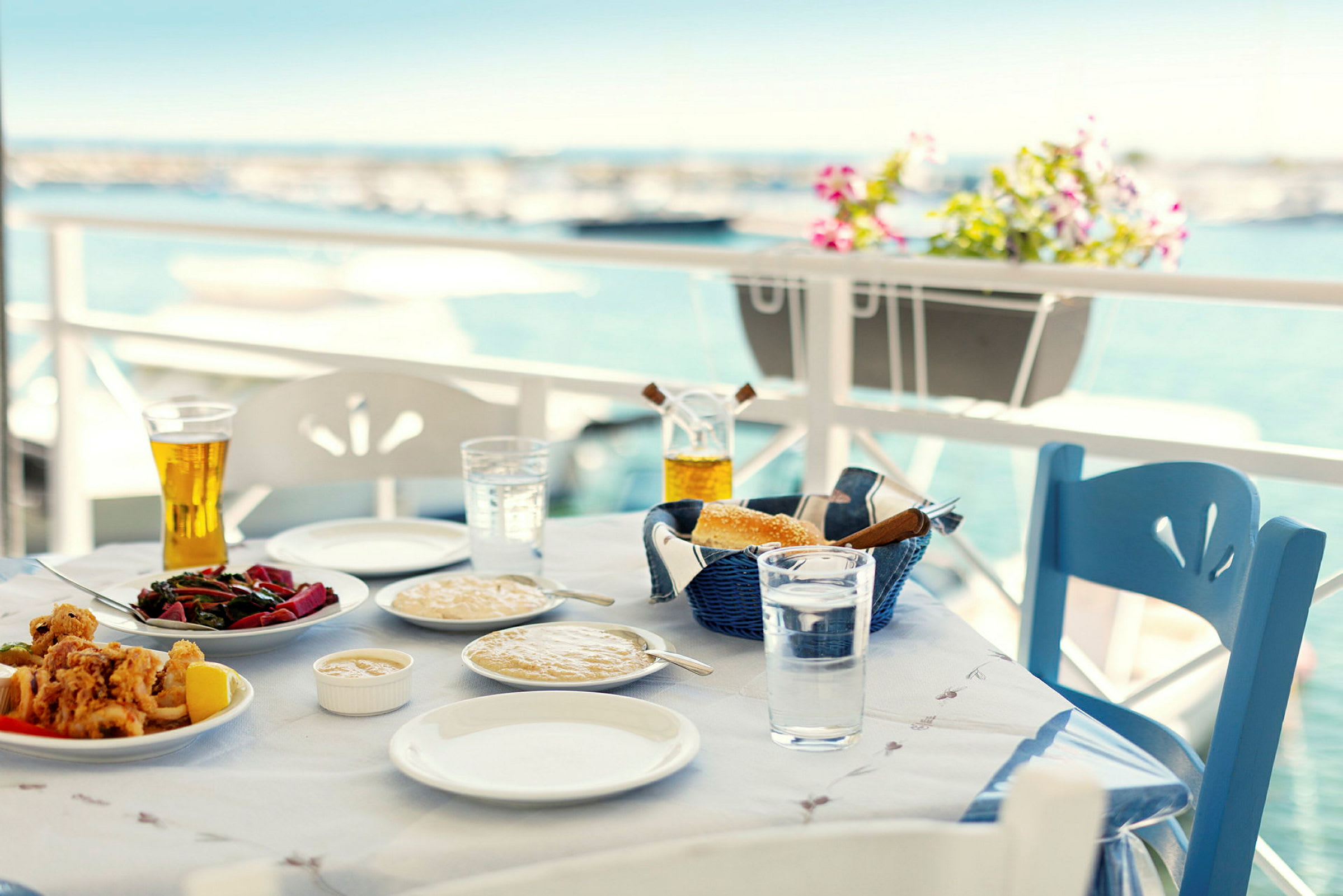 Ett dukat bord med mat och dryck vid en terrass med utsikt över havet. (AI-genererad text)
