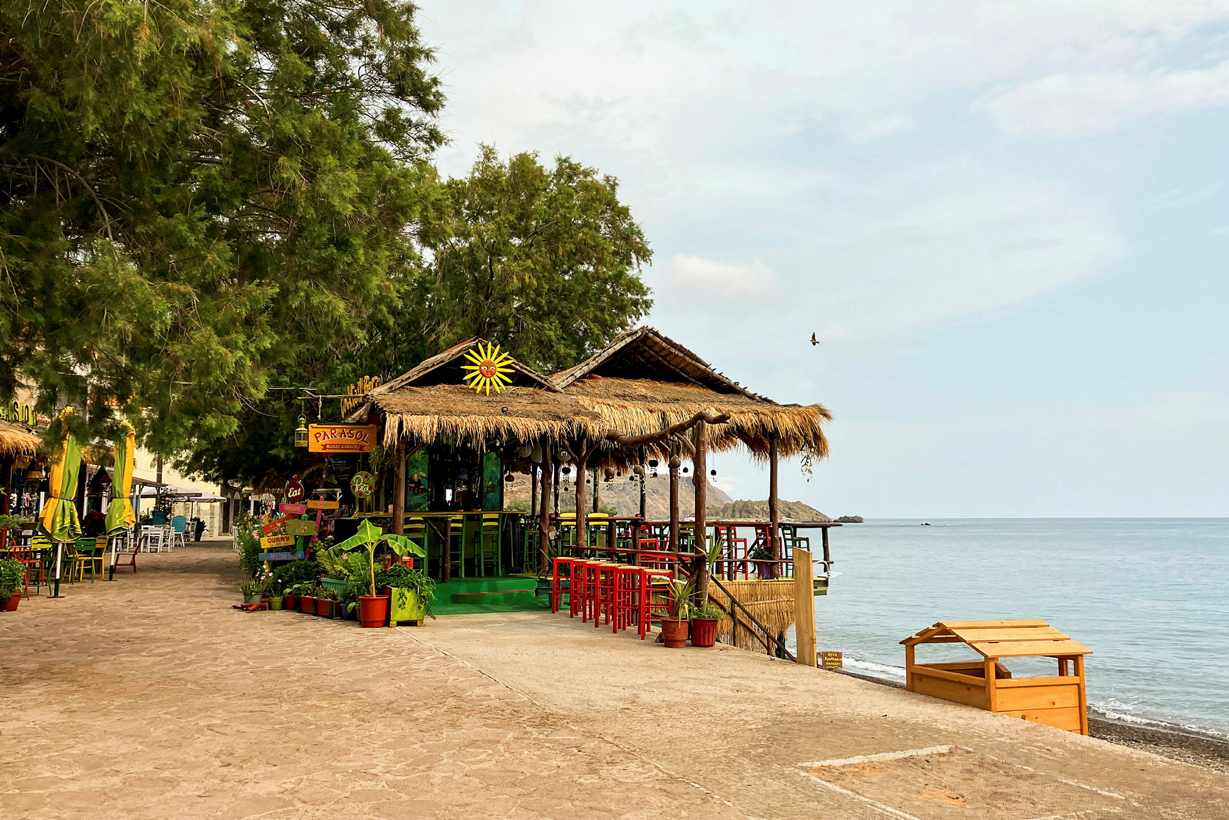 Strandnära café med halmtak och färgglada stolar. (AI-genererad text)