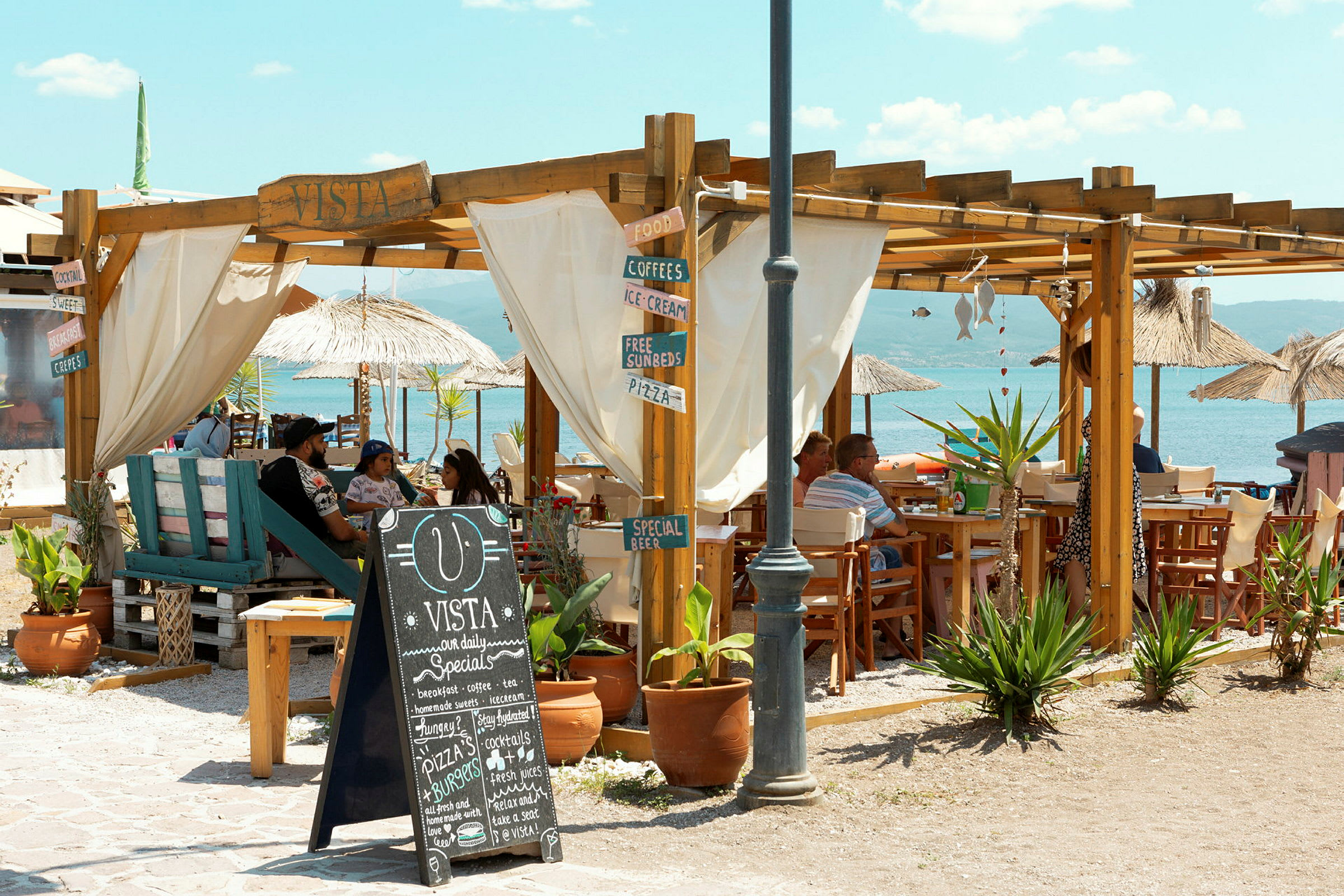Utomhusområde av ett strandcafé med träkonstruktioner och bord, nära havet. (AI-genererad text)