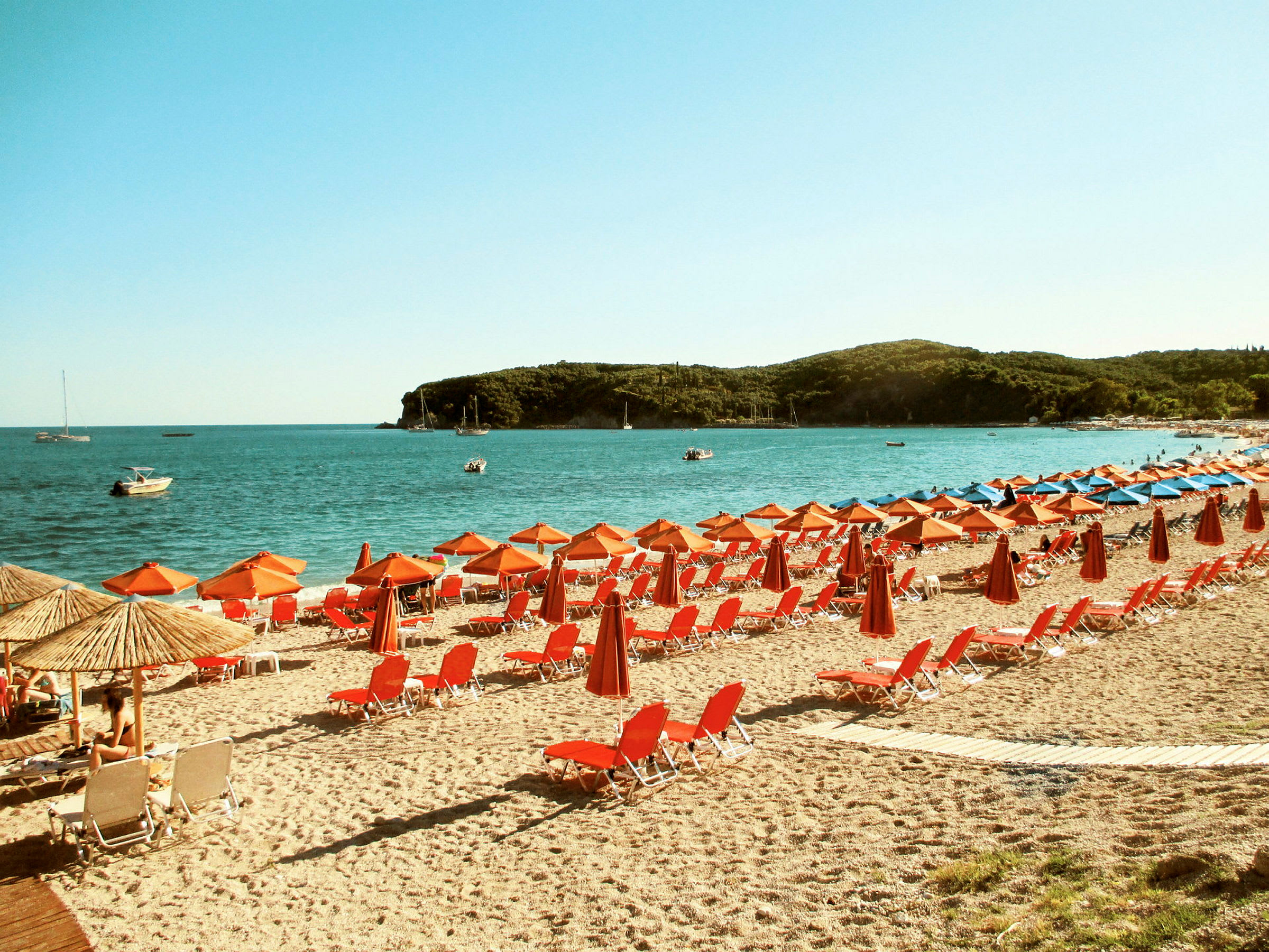 Strand med röda solstolar och parasoller vid kustlinjen. (AI-genererad text)