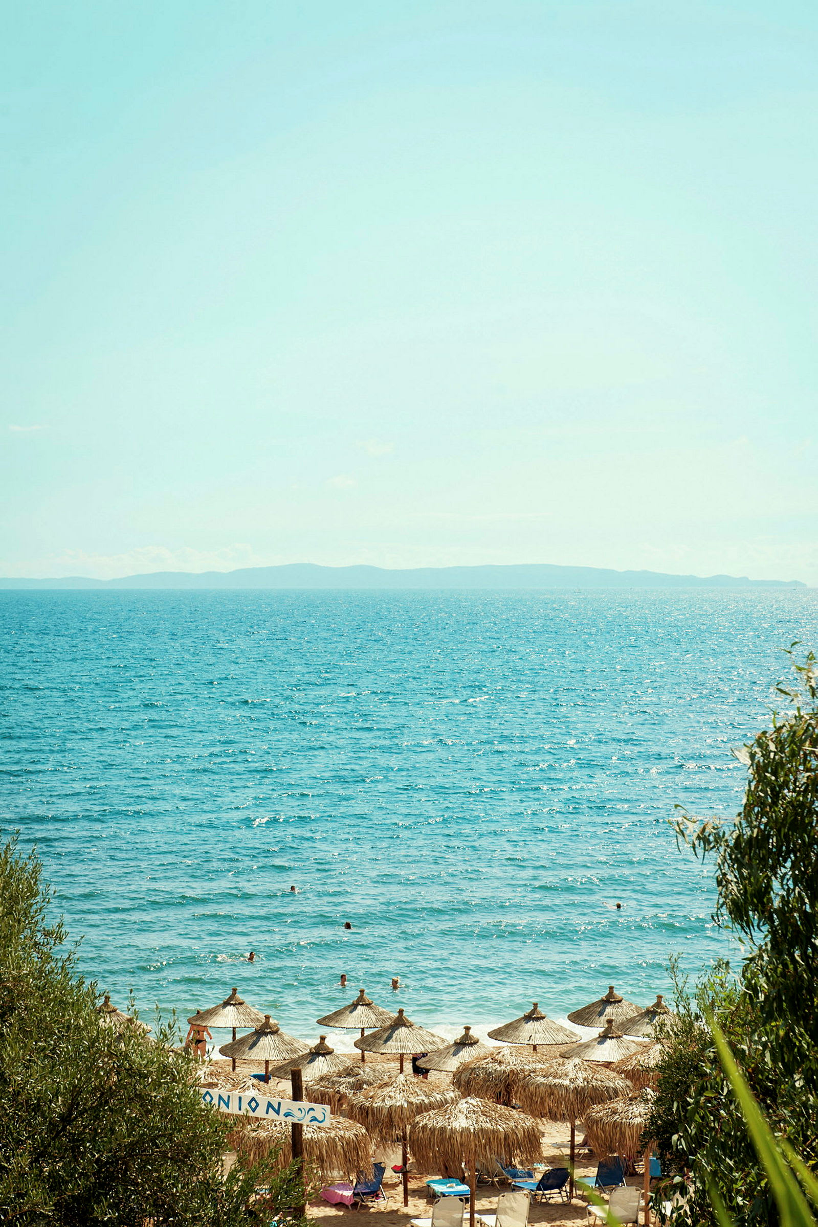 Vy över strand med parasoller och badande personer i havet. (AI-genererad text)