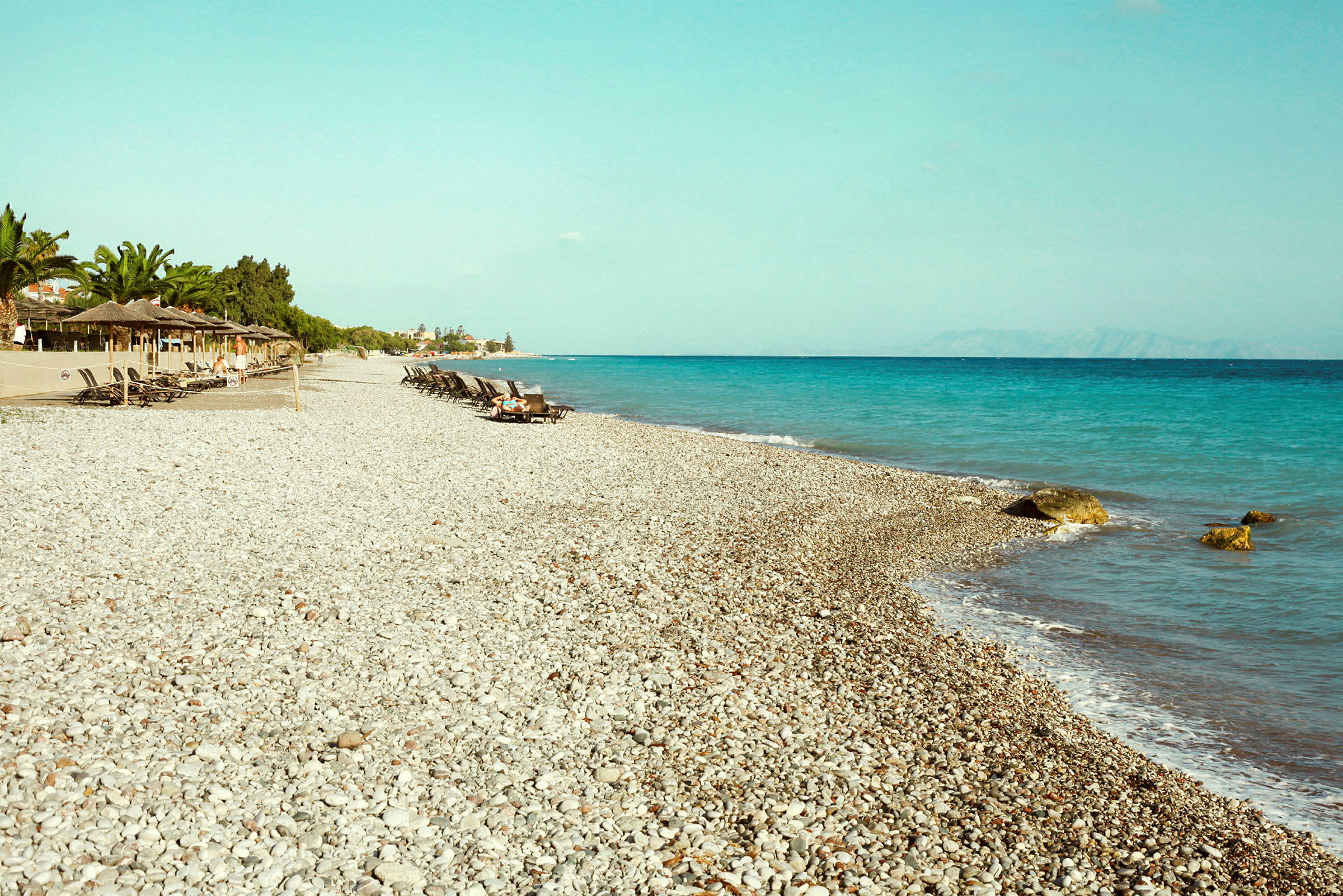 En stenstrand med solstolar och parasoller nära havet. (AI-genererad text)