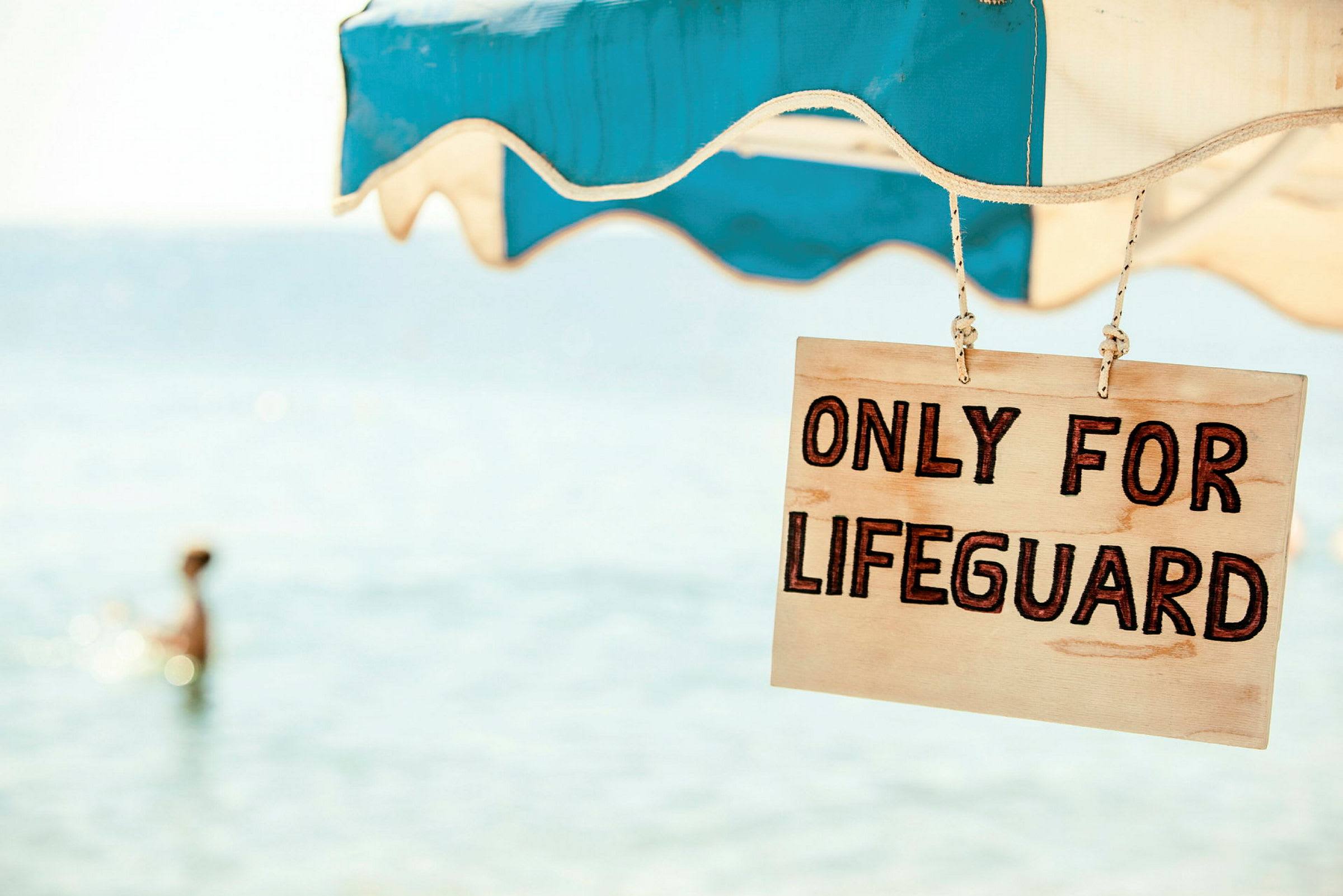 Skylt med texten 'Only for lifeguard' upphängd under ett parasoll nära havet. (AI-genererad text)