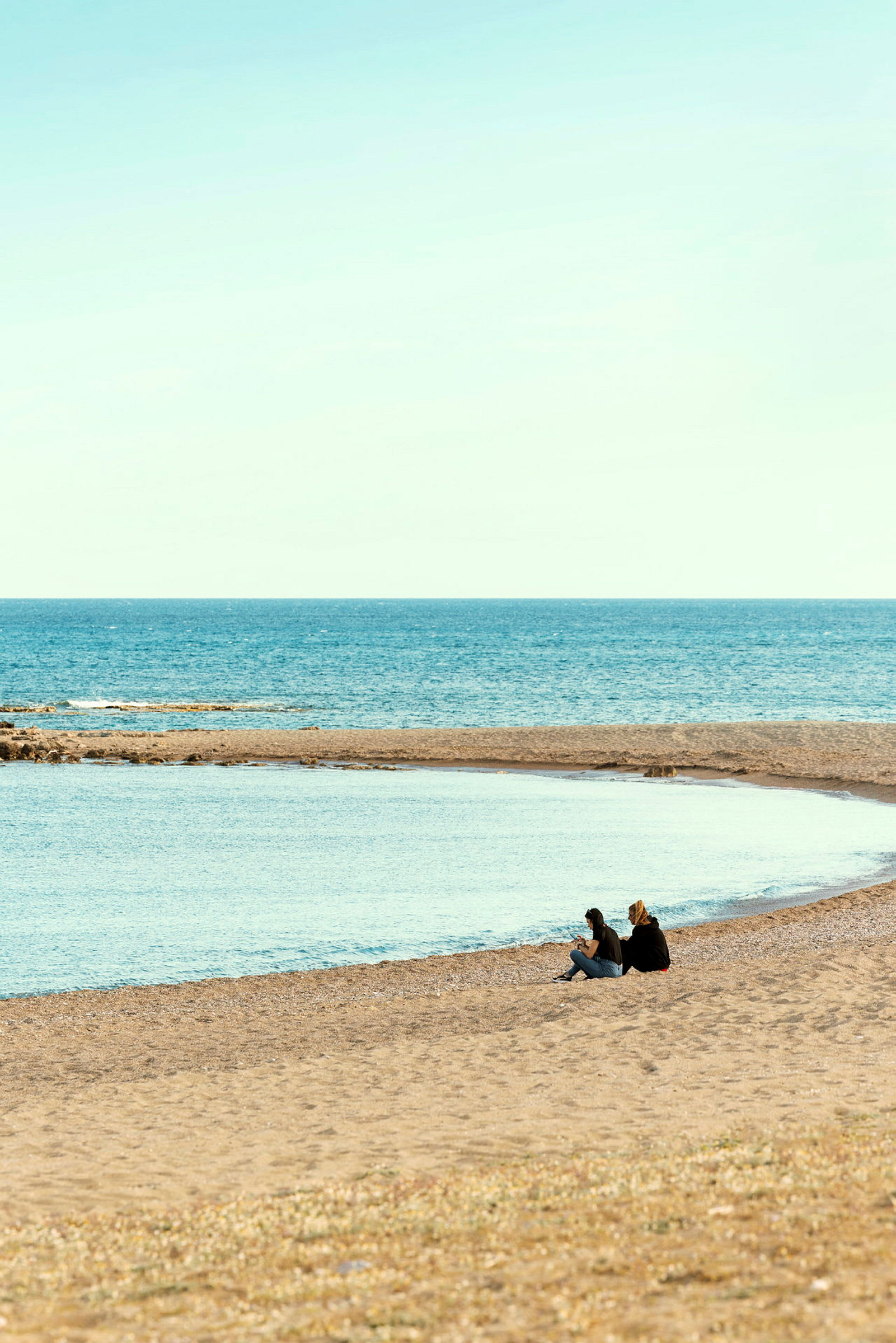 Två personer sitter på en strand nära havet under klar himmel. (AI-genererad text)