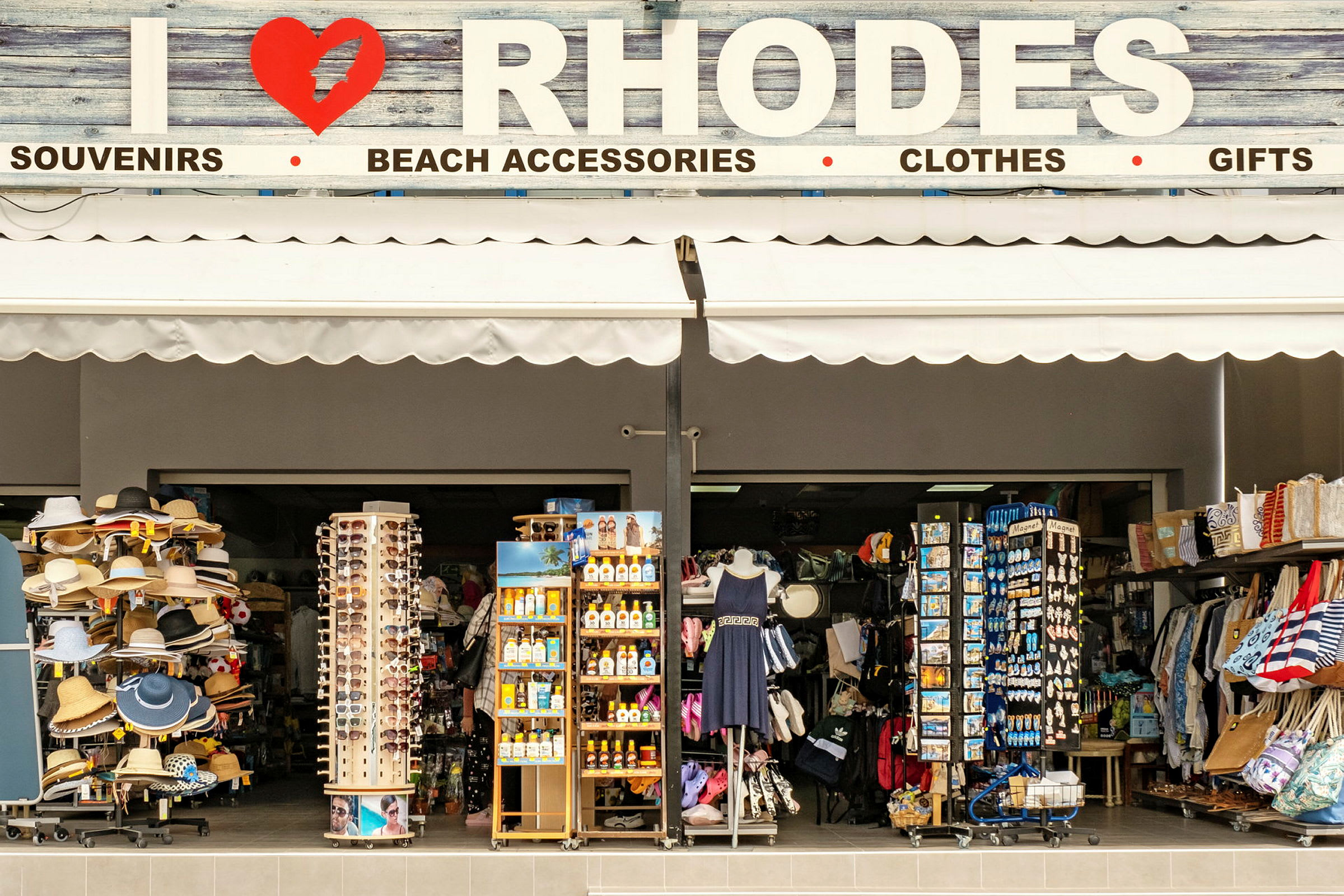 En butik som säljer souvenirer och strandtillbehör med skylten ovanför som säger "I ❤ RHODOS". (AI-genererad text)