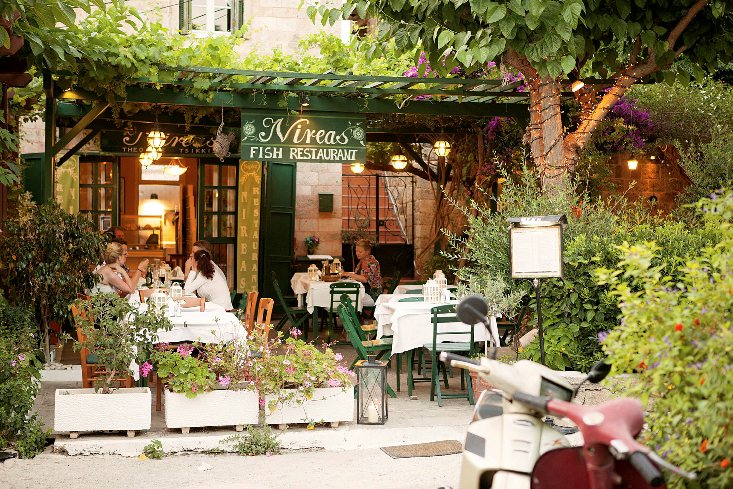 En restaurang utomhus med gröna möbler och växter runt omkring. (AI-genererad text)