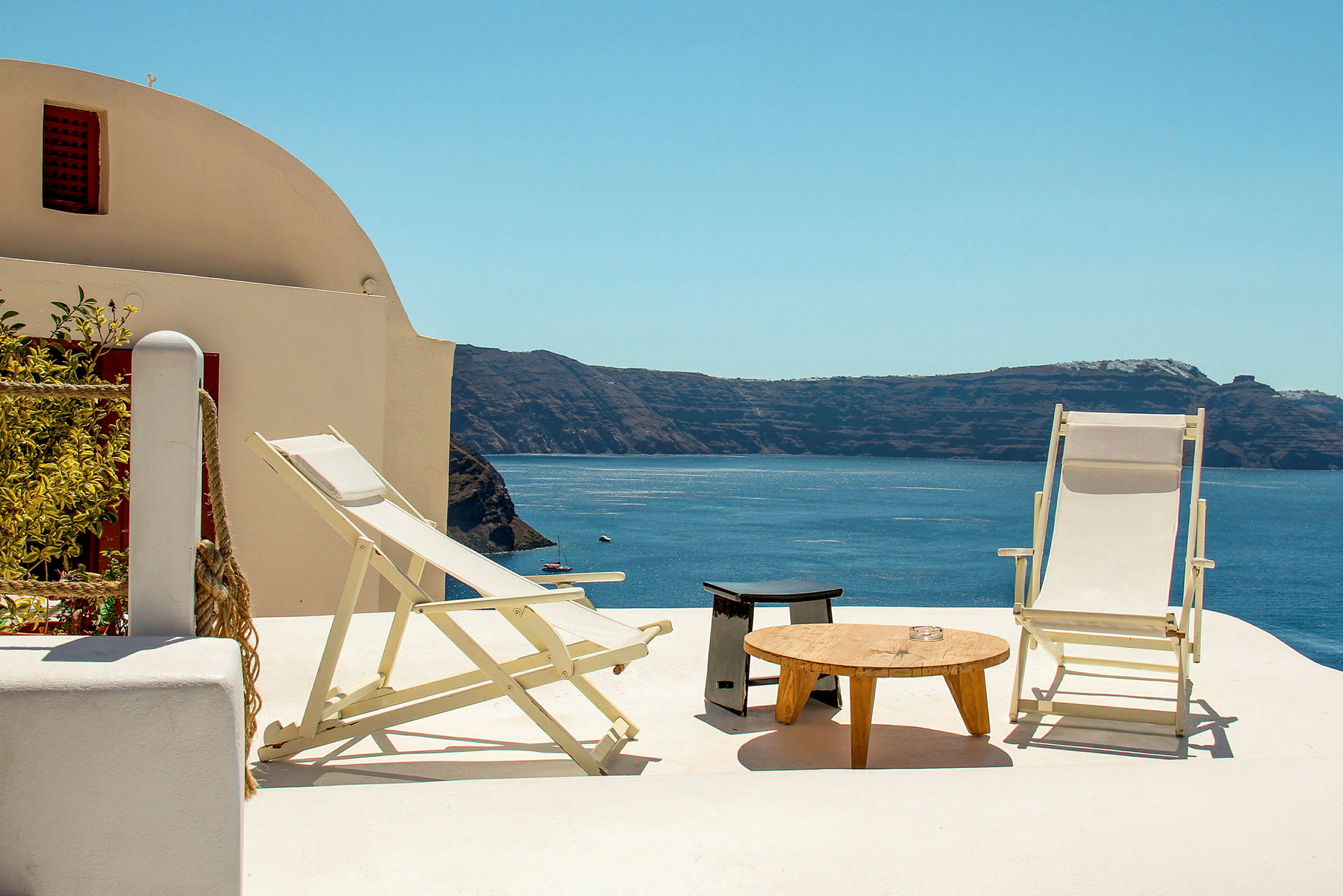 Två solstolar och ett bord på en terrass med utsikt över havet och klippor. (AI-genererad text)