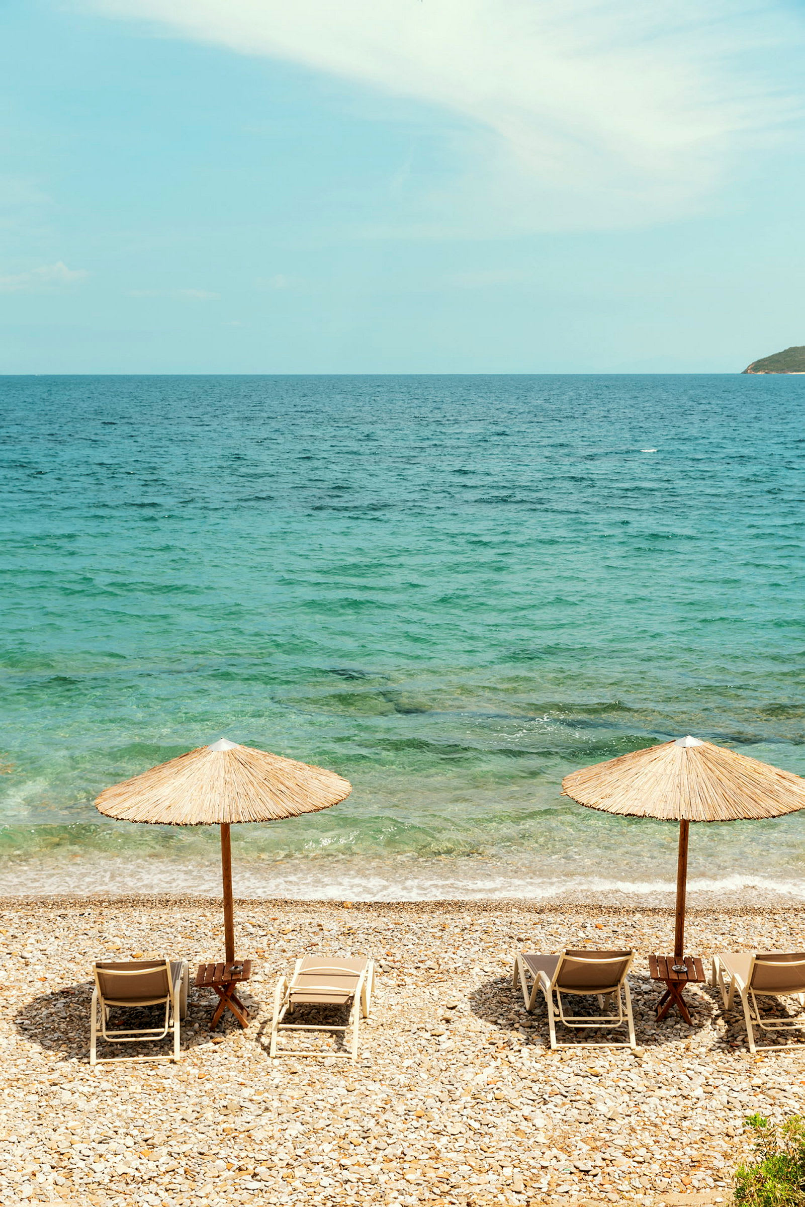 Två solstolar med parasoller på en stenig strand vid havet. (AI-genererad text)