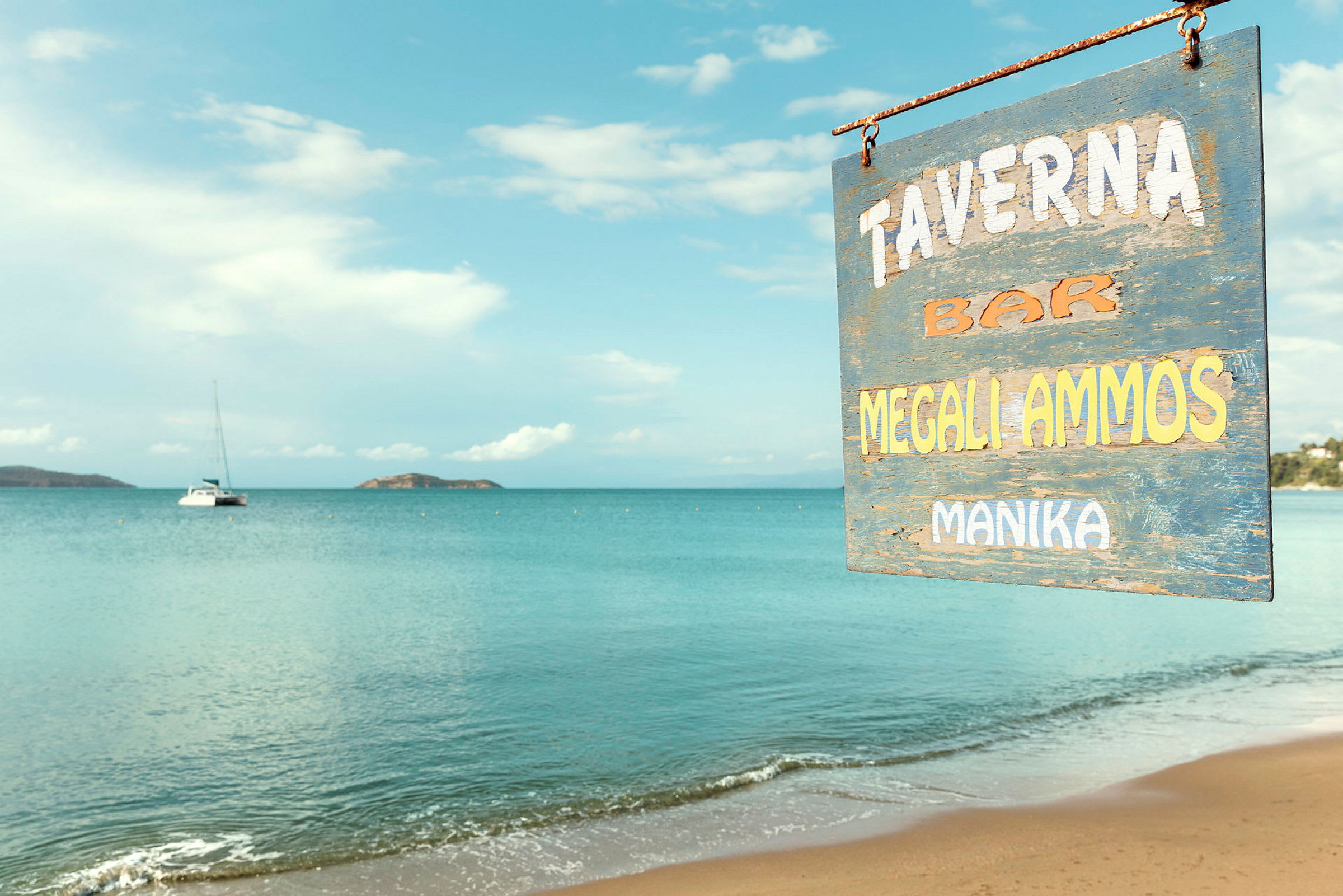 Skylt för en taverna vid en sandstrand med lugnt hav i bakgrunden. (AI-genererad text)