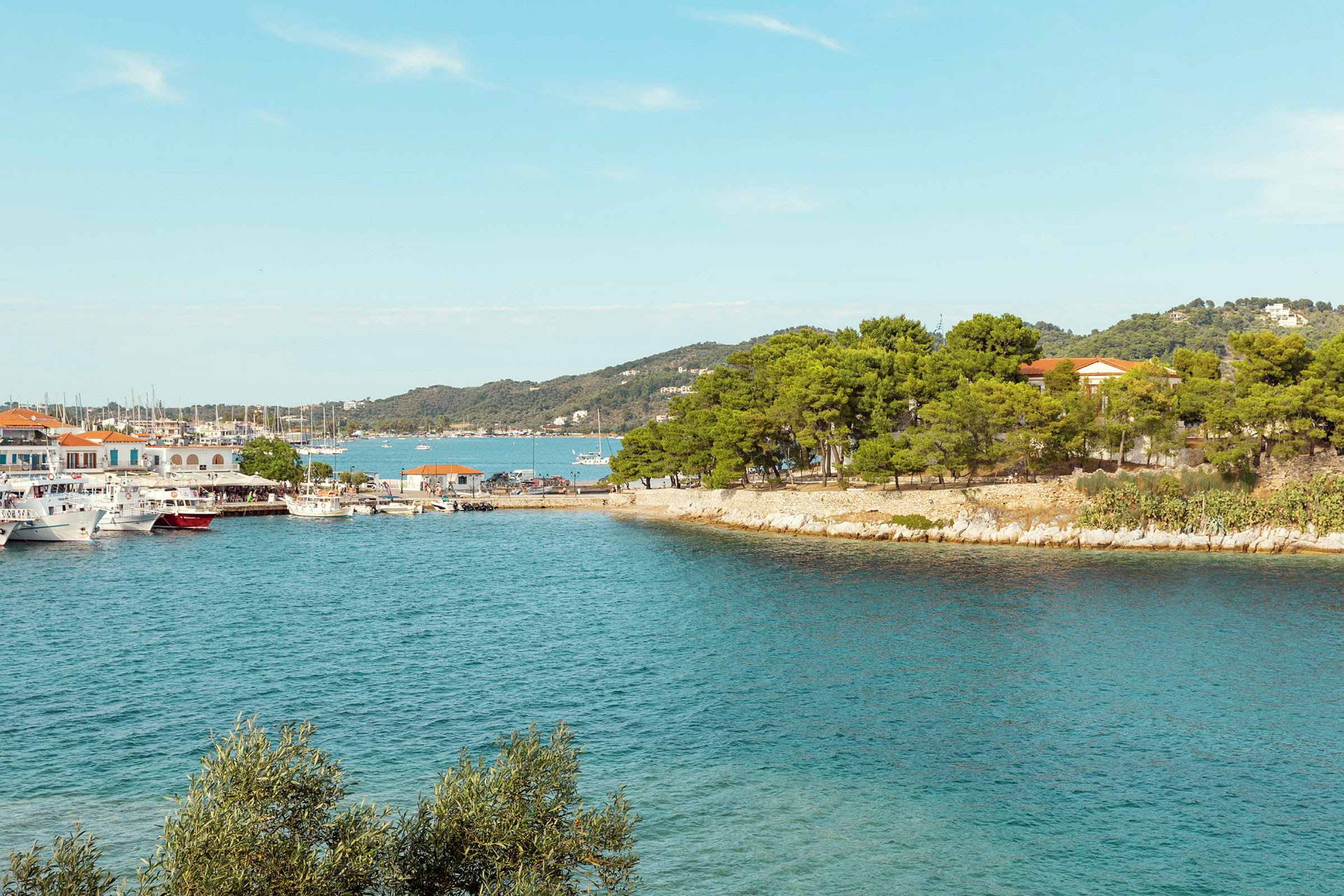 En hamn med båtar omgiven av gröna träd och klippor. (AI-genererad text)