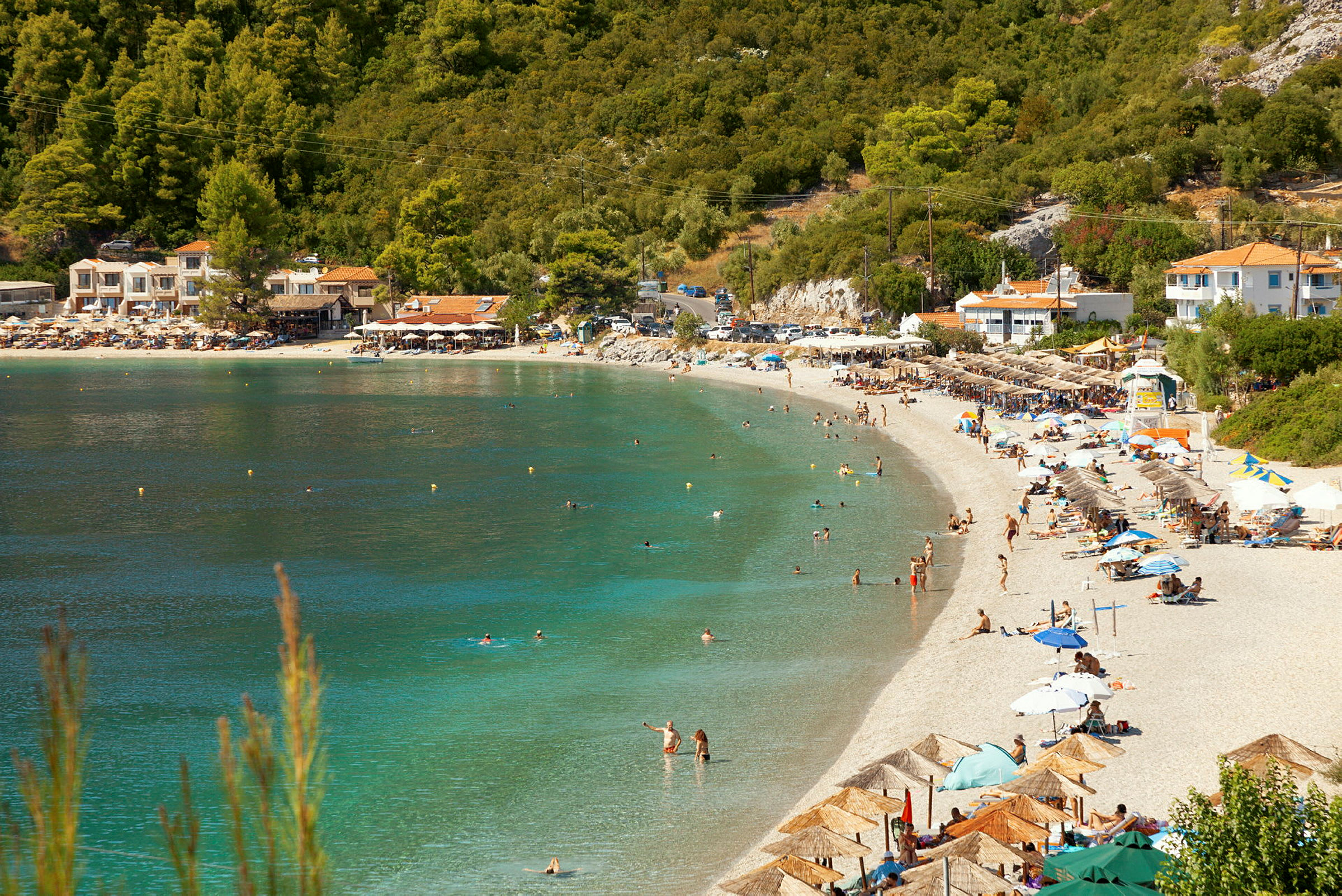 Strand med turkost vatten, besökare och parasoller med en grönskande bakgrund. (AI-genererad text)