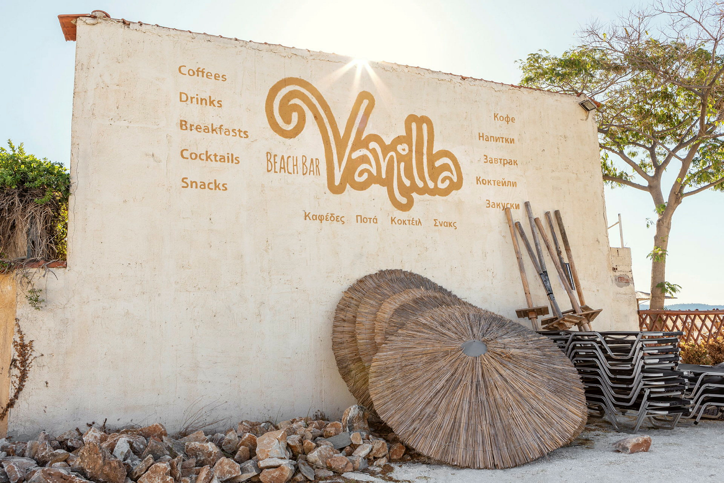 En vägg med texten "Vanilla Beach Bar" tillsammans med erbjudanden, samt solparasoller och stolar bredvid. (AI-genererad text)