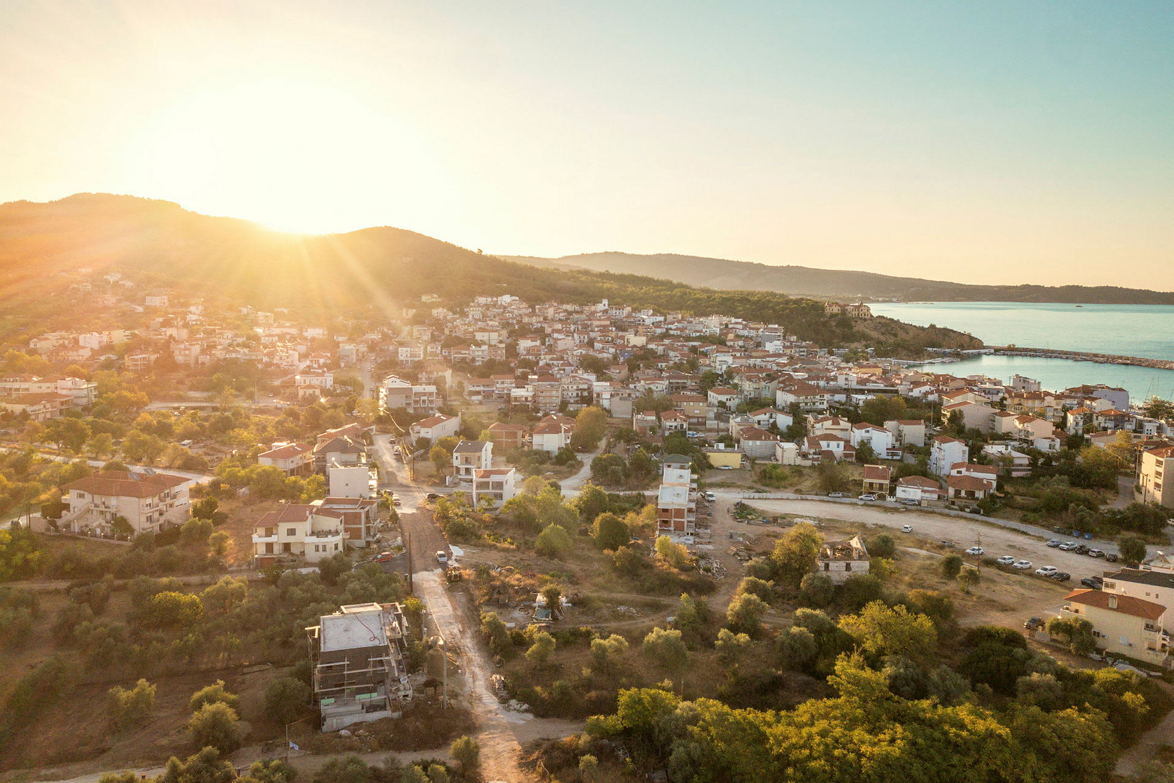 Solnedgång över en mindre stad med hus och gröna områden, havet syns i bakgrunden. (AI-genererad text)