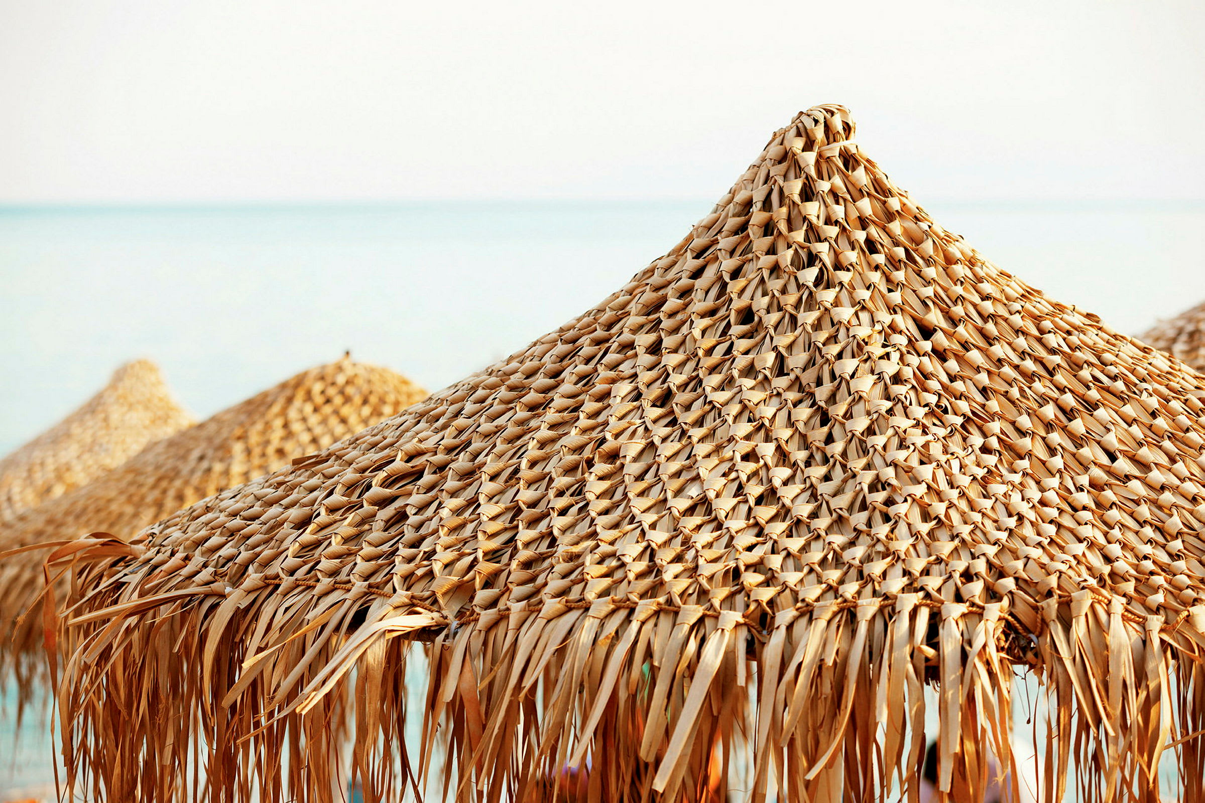 Solparasoller av flätad strå vid en strand. (AI-genererad text)