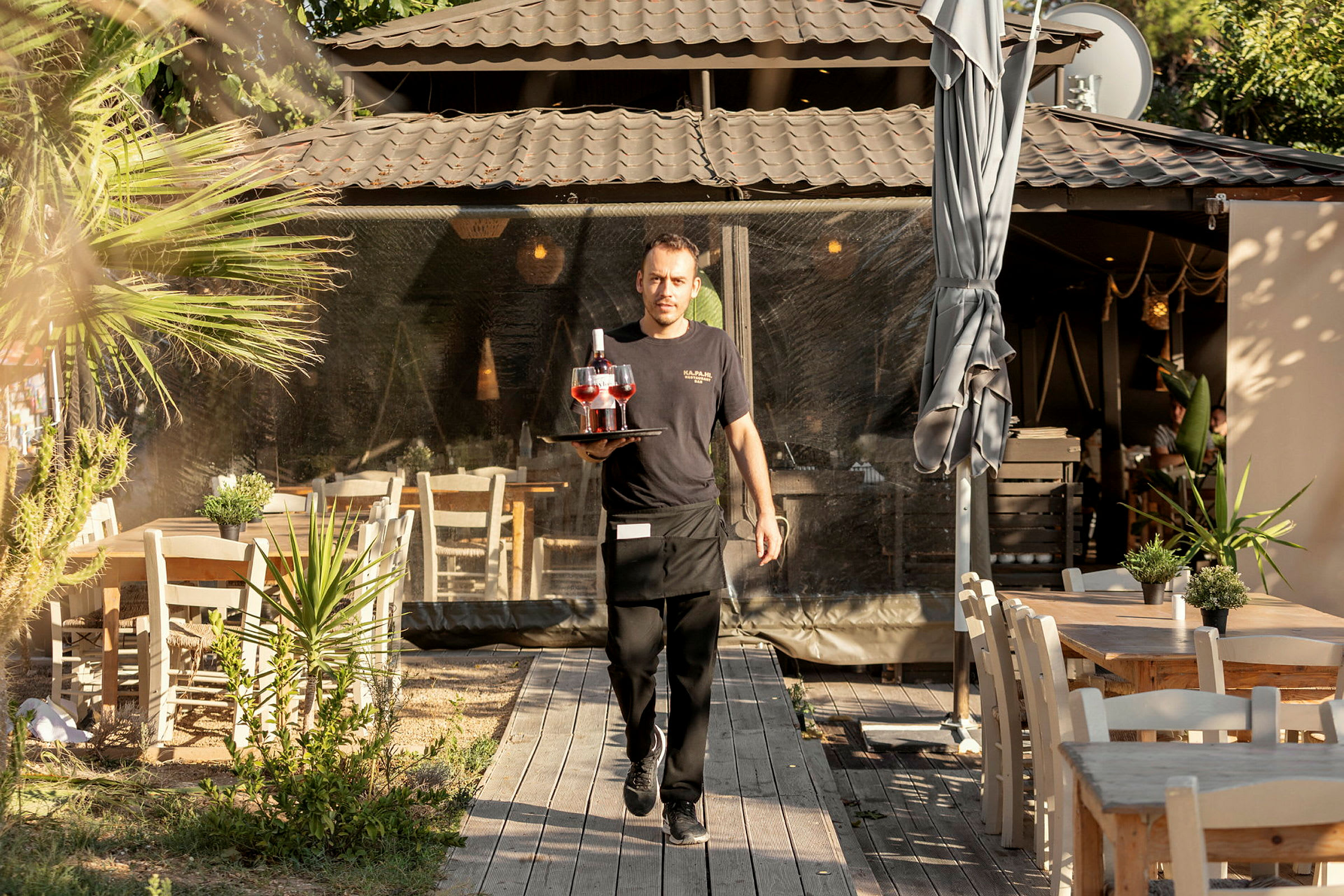 En servitör bär bricka med drycker i en utomhusrestaurang. (AI-genererad text)