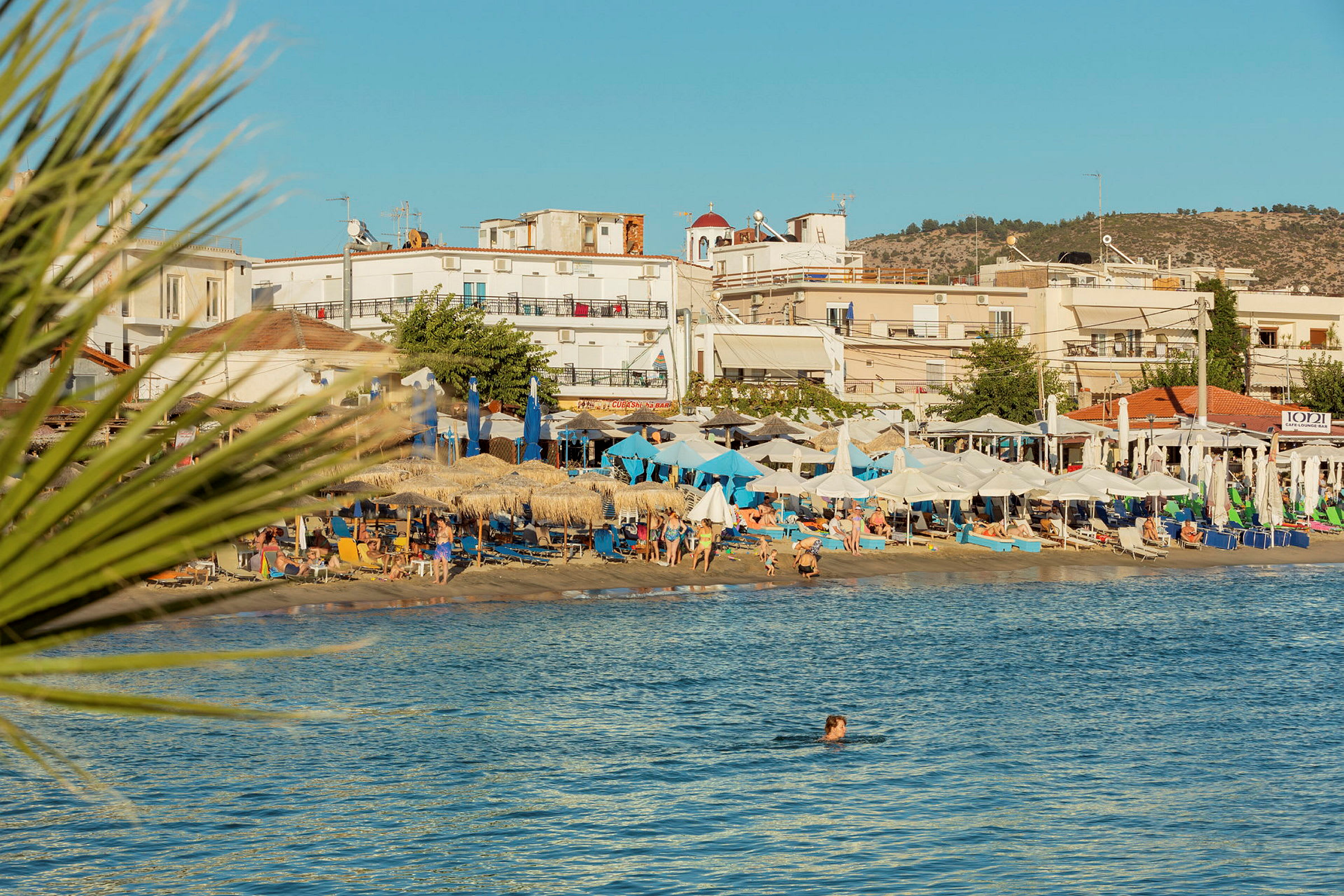 En strand med parasoller, solstolar och badande gäster nära byggnader. (AI-genererad text)