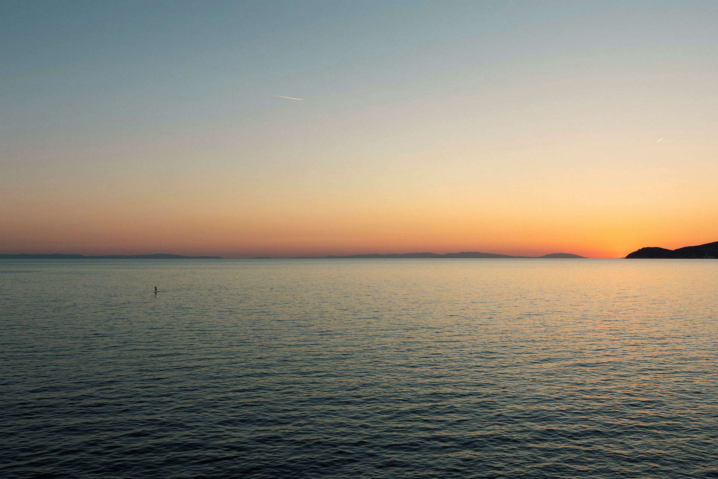 En person står på en paddleboard på stilla havsvatten vid solnedgången. (AI-genererad text)