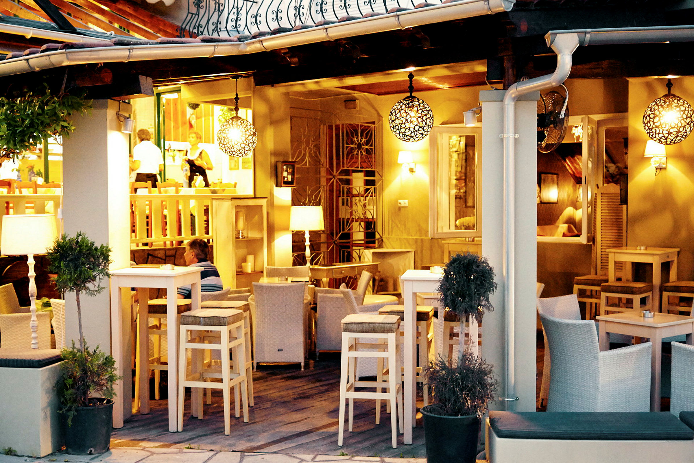 En utomhusrestaurang med höga barstolar, bord och belysning i kvällsljus. (AI-genererad text)