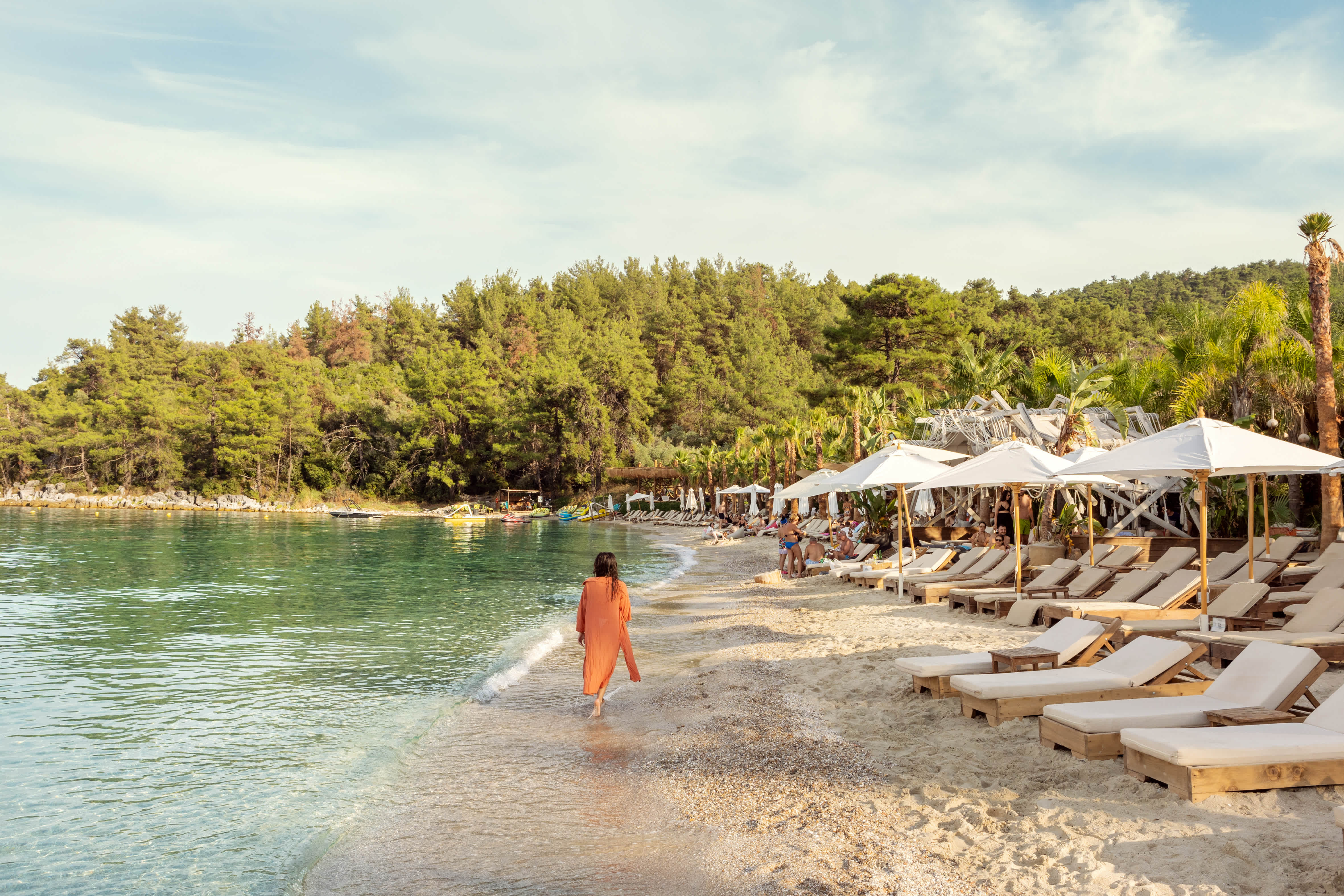 En person går längs en sandstrand med solstolar och parasoll på höger sida och havet på vänster sida. (AI-genererad text)