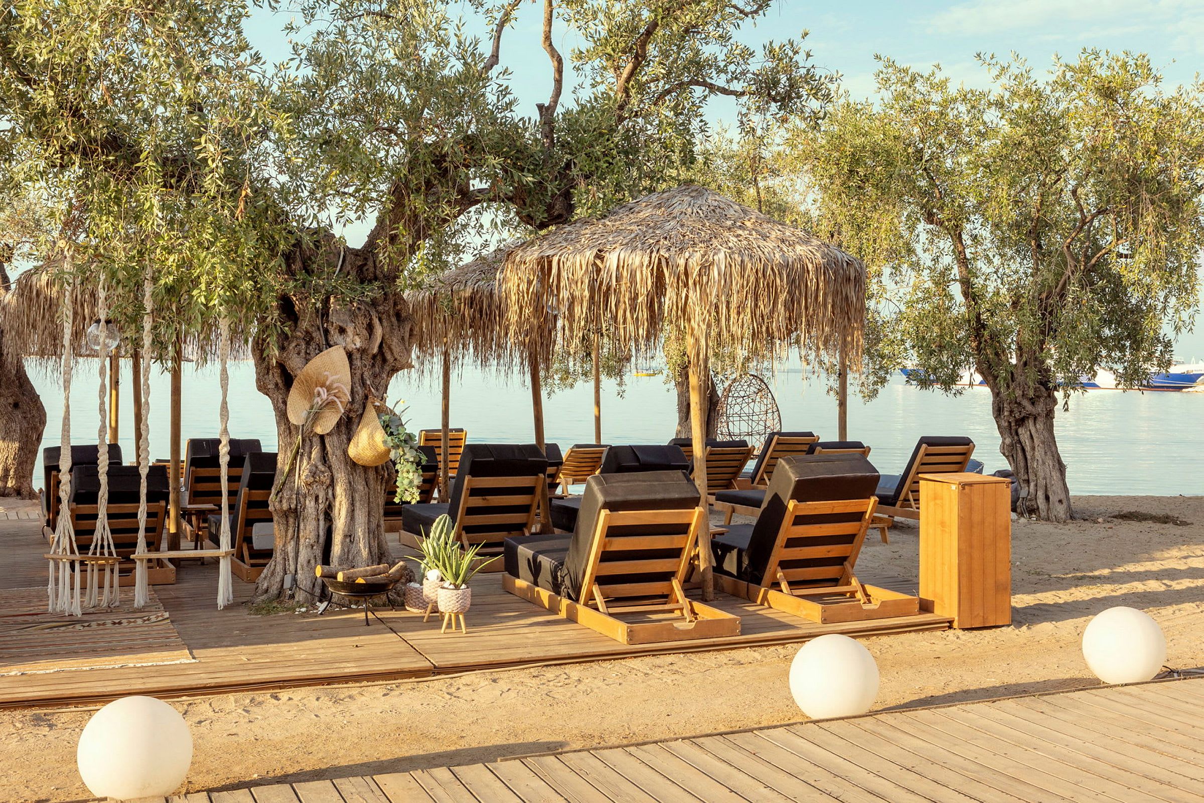 Trästolar med dynor under parasoller på en strand med träd. (AI-genererad text)