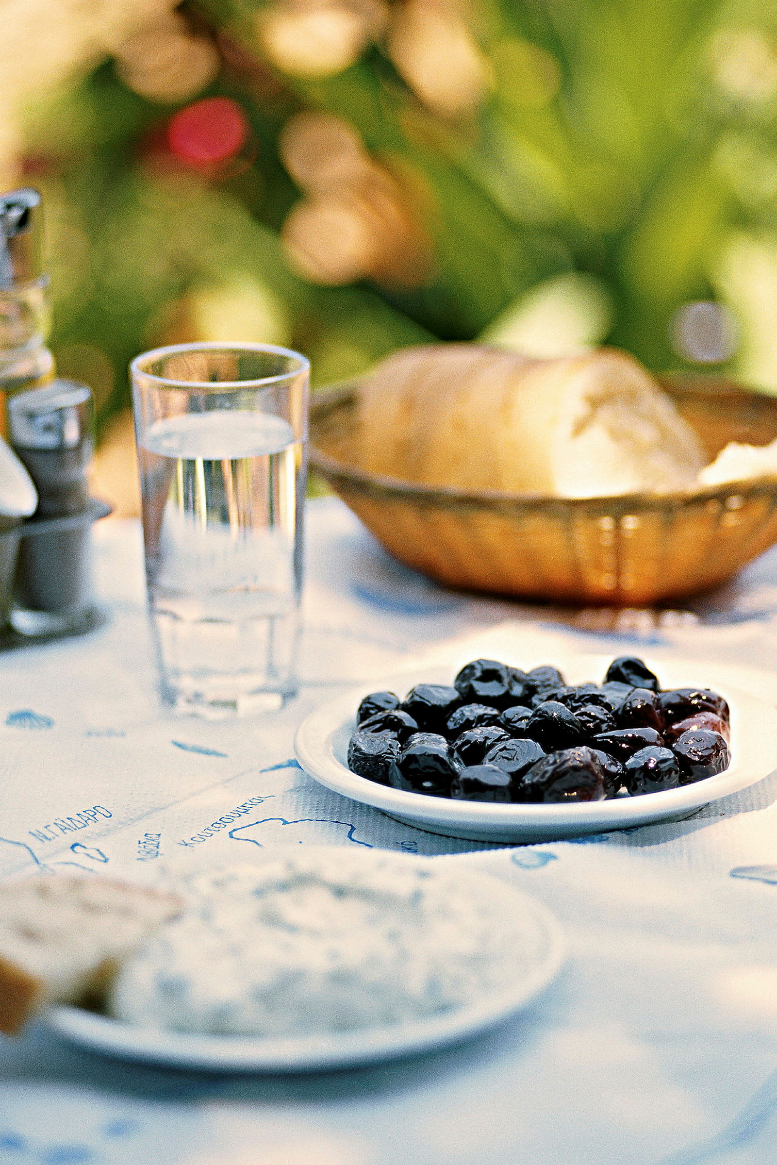 Tallrik med svarta oliver, ett glas vatten och ett bröd på ett bord. (AI-genererad text)