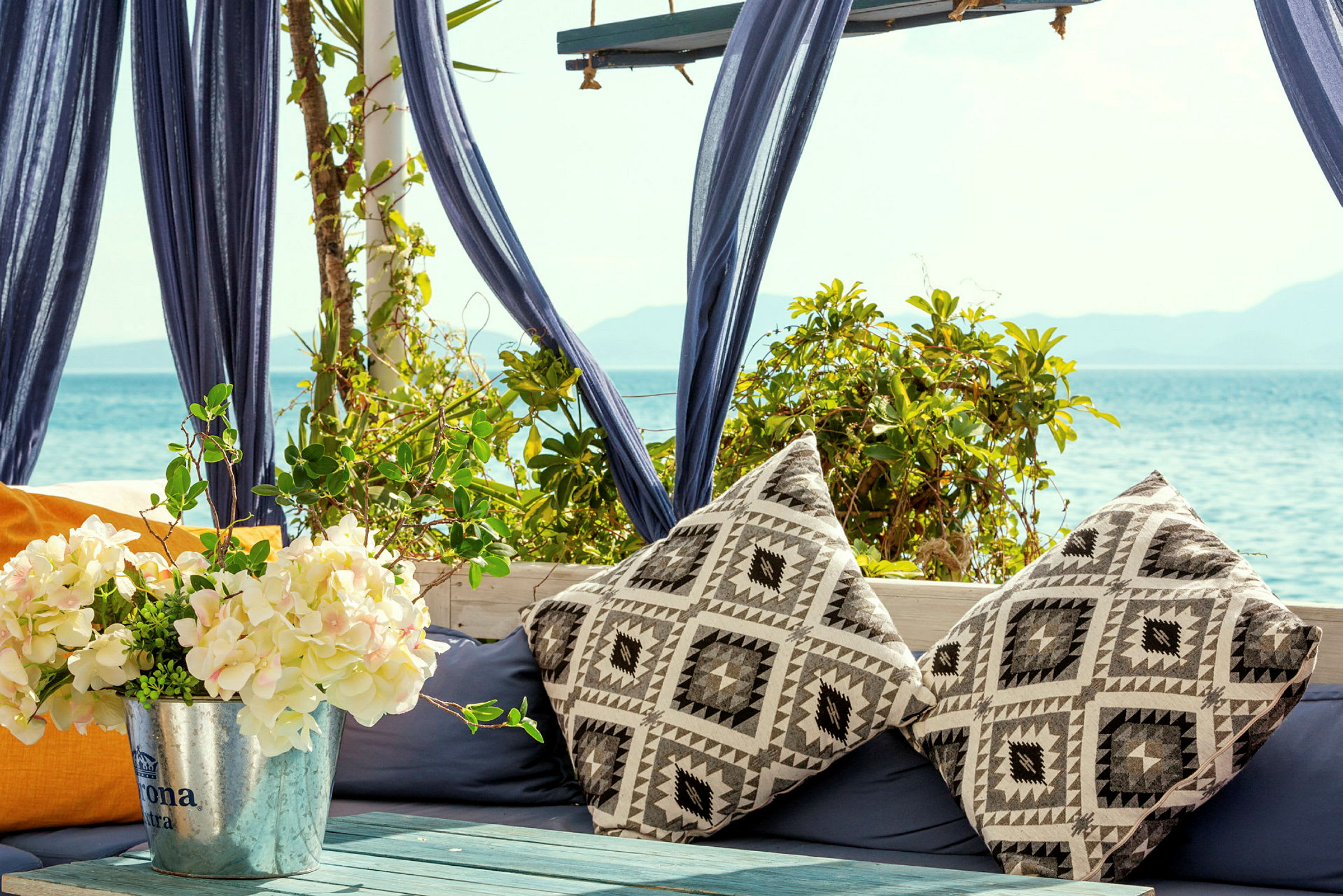 Sittplats vid havet med kuddar och blomdekor. (AI-genererad text)
