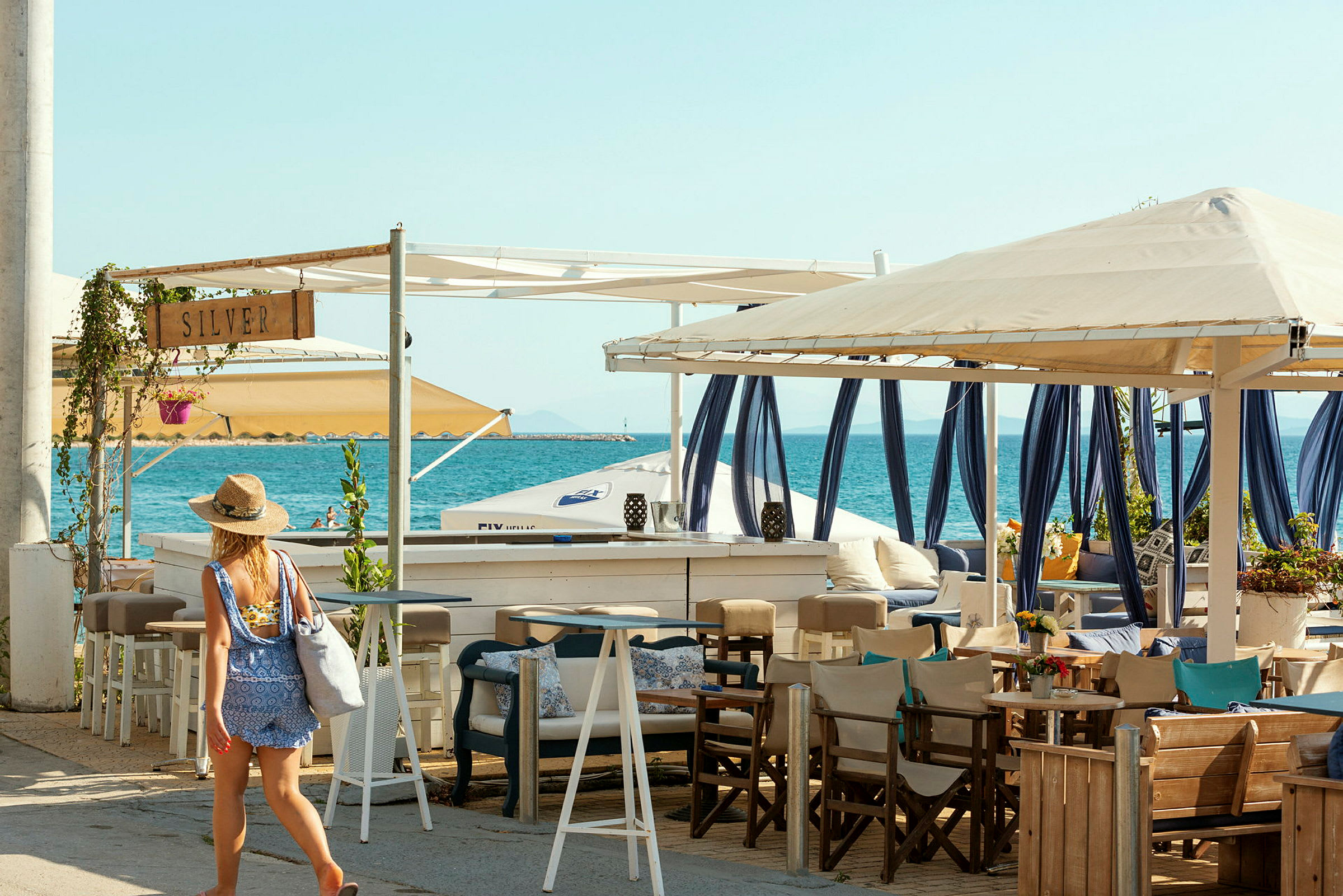Bild på en person som går vid en strandbar med sittplatser och hav i bakgrunden. (AI-genererad text)