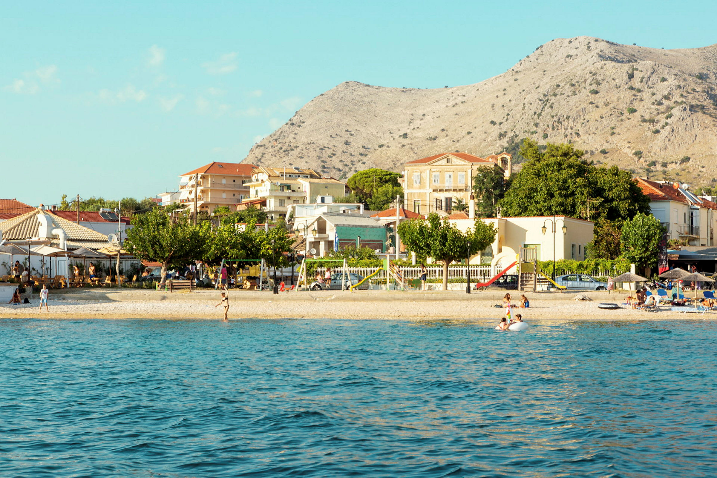 Utsikt över en strand med byggnader och berg i bakgrunden. (AI-genererad text)