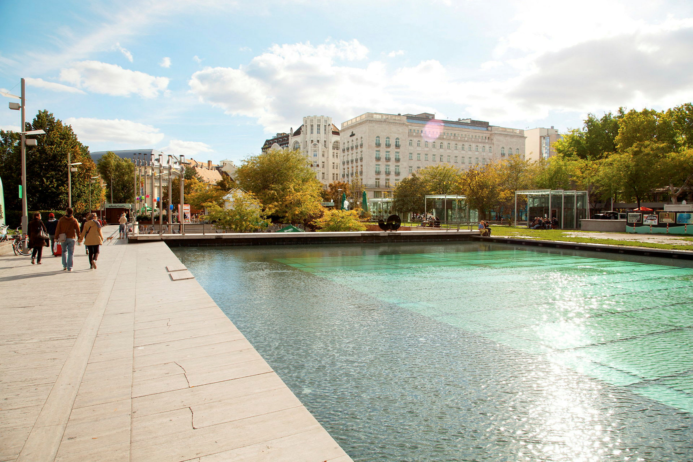 En promenadväg vid en modern park med en reflekterande vattenyta och grönska. (AI-genererad text)