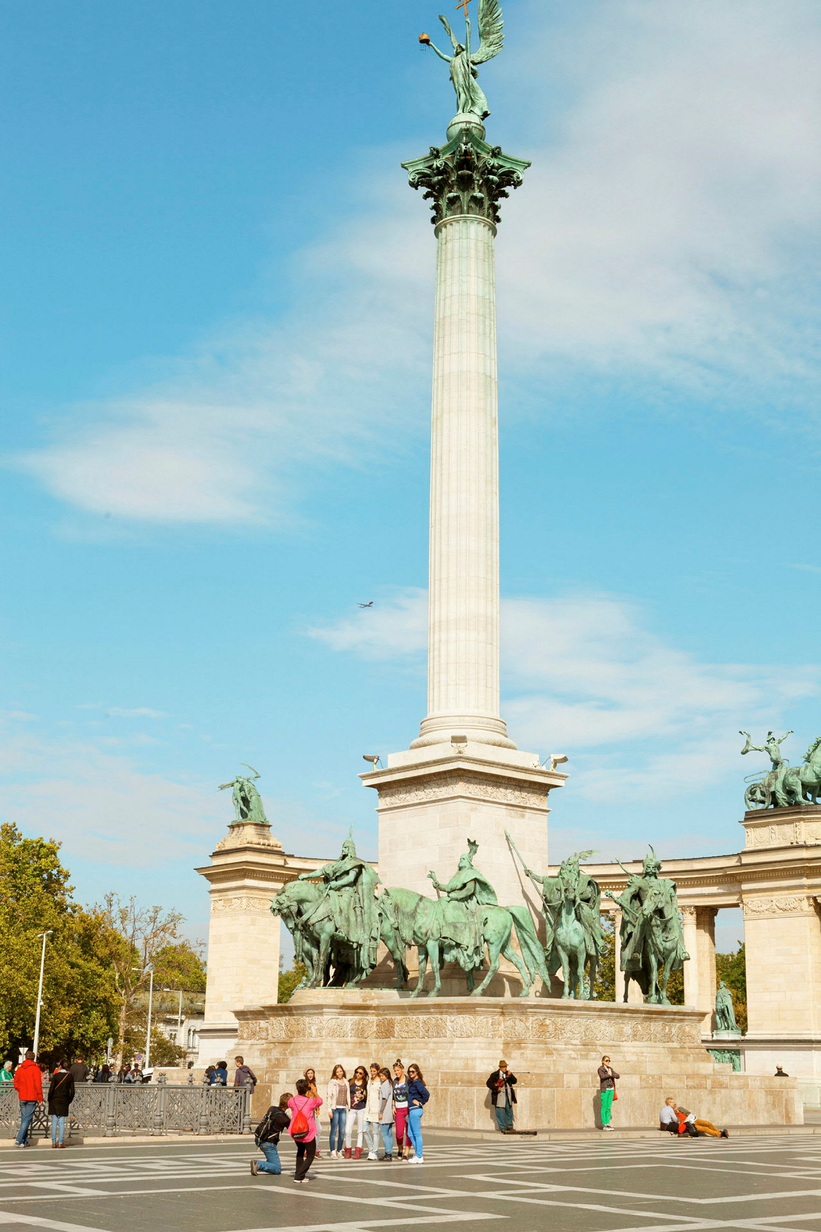 En hög kolonn med en staty ovanpå, omgiven av flera ryttarskulpturer vid ett monument på ett öppet torg. (AI-genererad text)