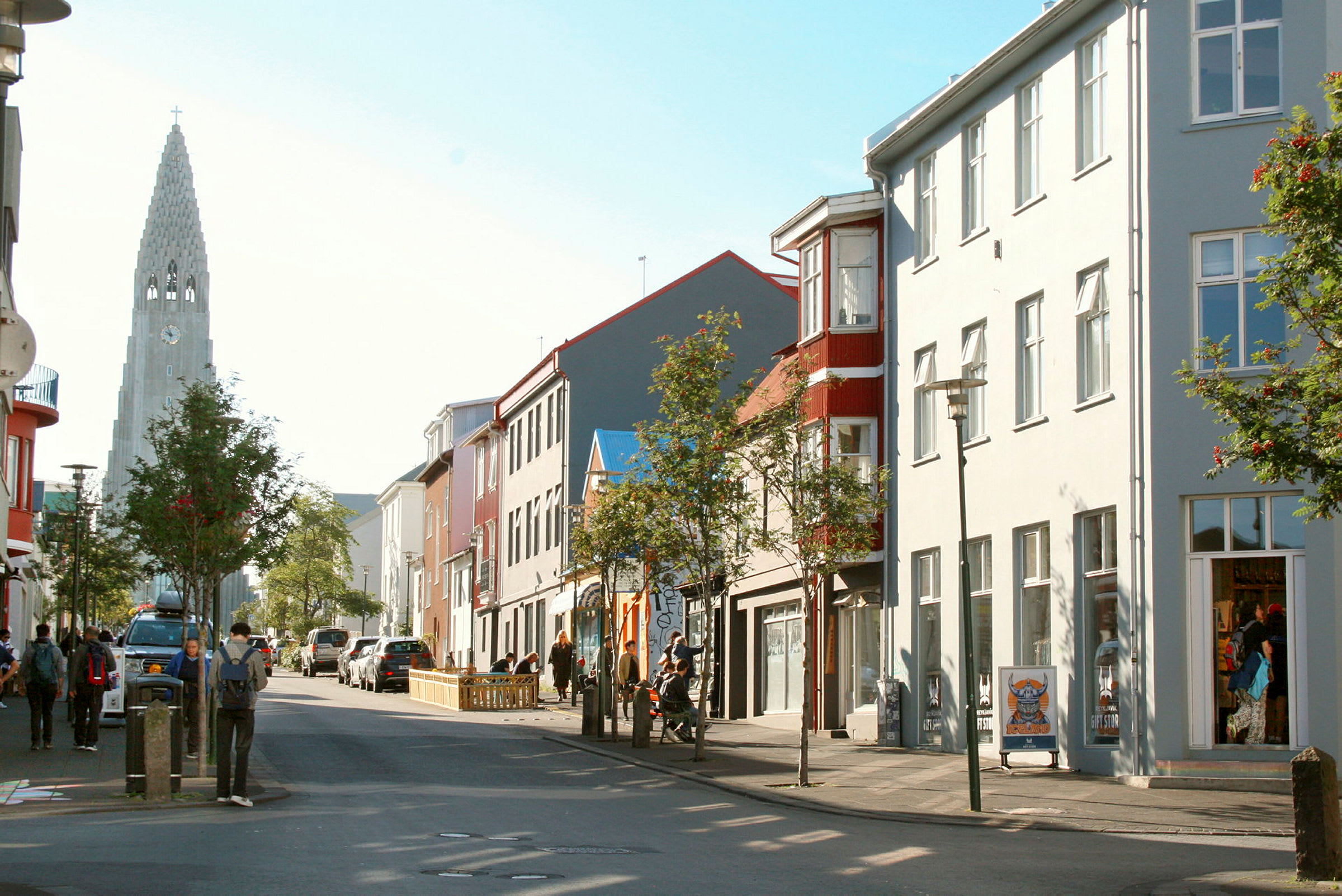 En gata med människor, byggnader och en kyrka med spira i bakgrunden. (AI-genererad text)