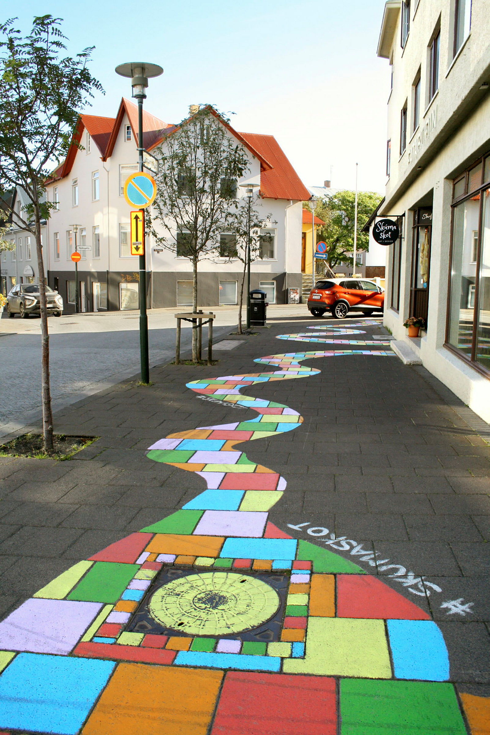 En färgglad målning täcker trottoaren och skapar ett mönster som går längs en gata med hus och träd. (AI-genererad text)