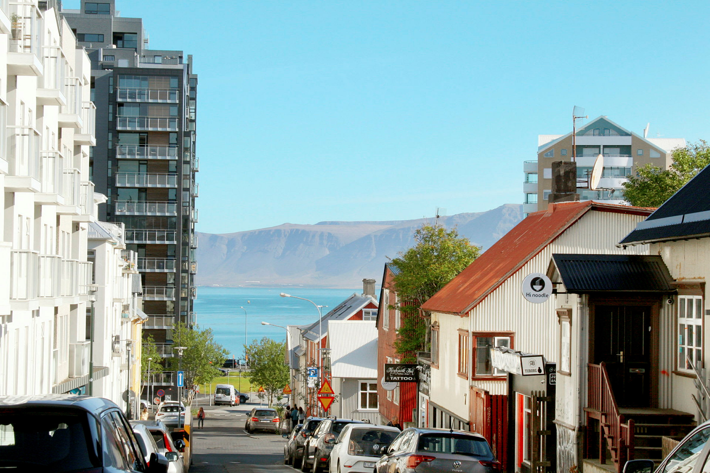 En gata i en stad med byggnader på båda sidor och utsikt över havet och berg i bakgrunden. (AI-genererad text)