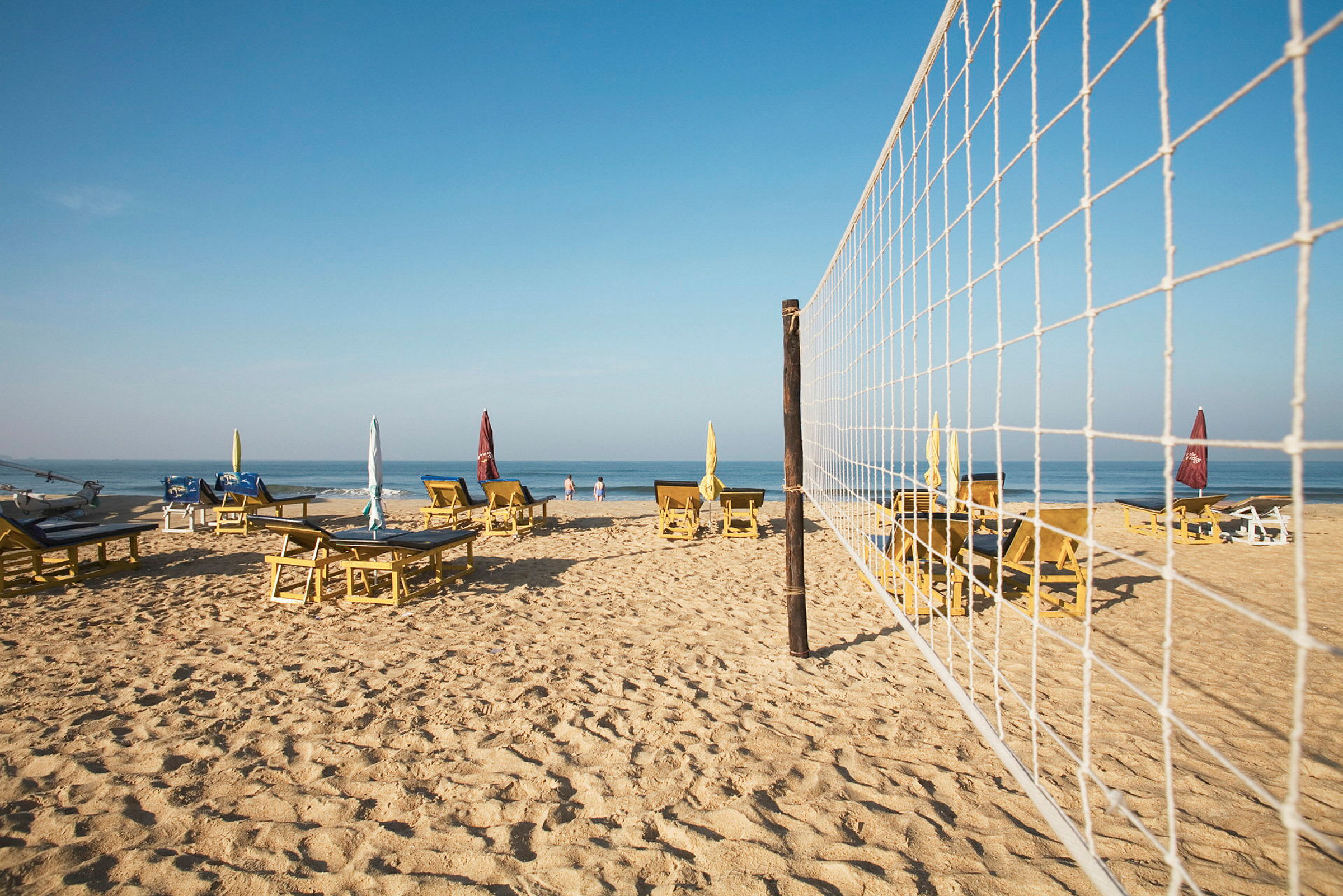 Strand med solstolar, parasoller och ett volleybollnät. (AI-genererad text)
