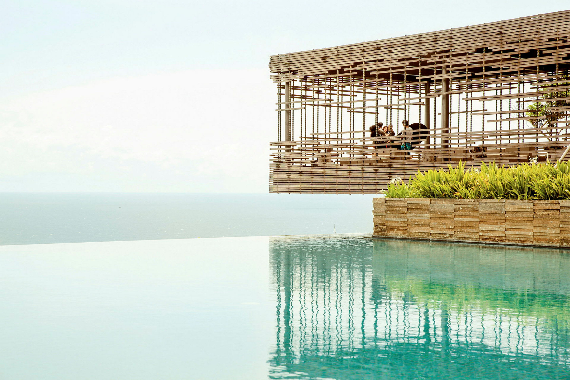 En utsikt över en infinitypool med havet i bakgrunden och en träpaviljong som svävar vid kanten. (AI-genererad text)