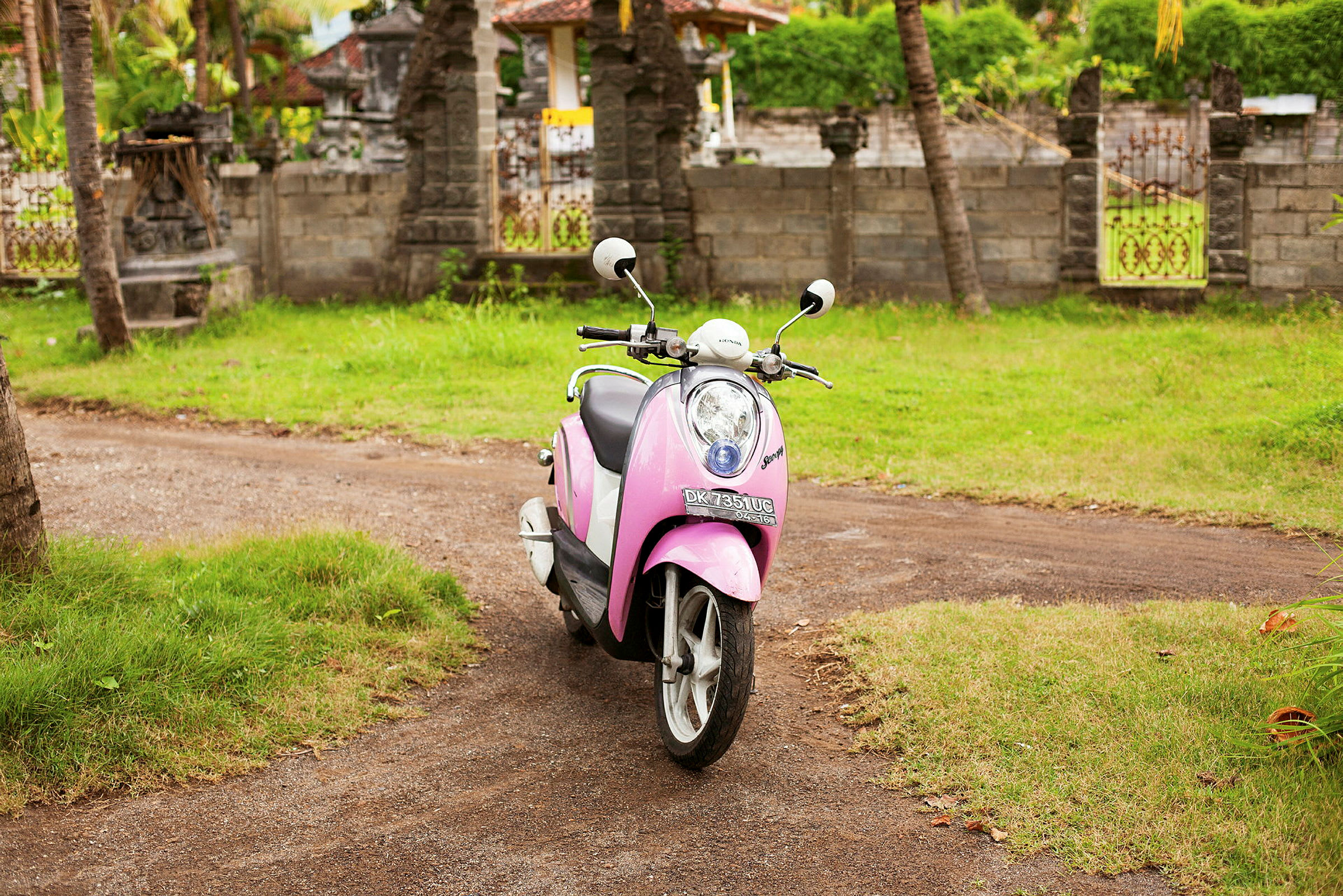 En rosa scooter står parkerad utomhus på en grusväg. (AI-genererad text)