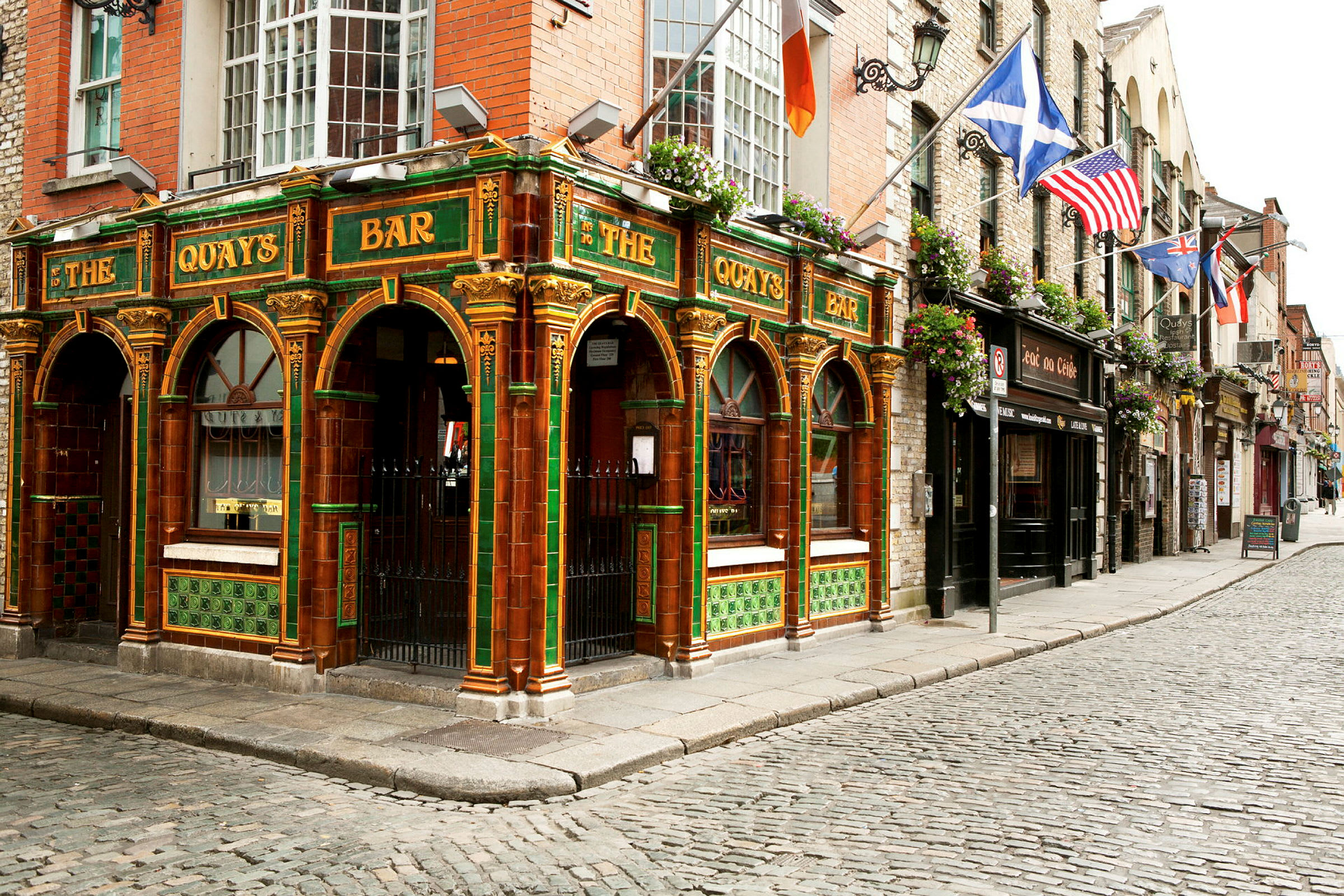 En färgglad pub med grön och orange dekor i traditionell stil ligger vid en kullerstensgata. (AI-genererad text)