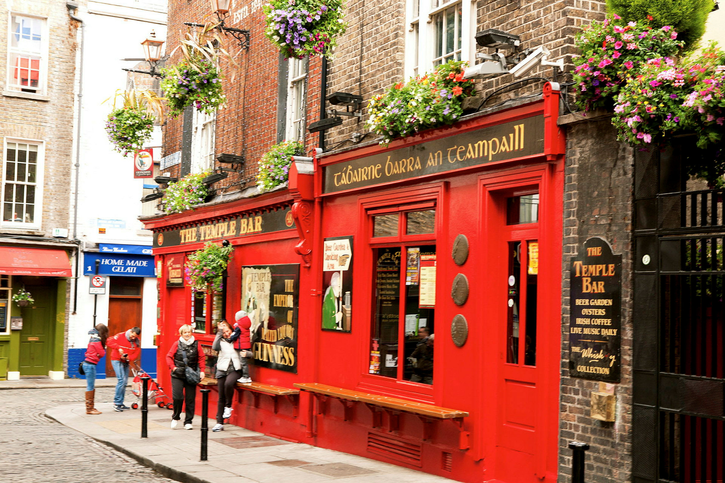 En röd byggnad med skylten 'The Temple Bar' med blomlådor och människor utanför. (AI-genererad text)