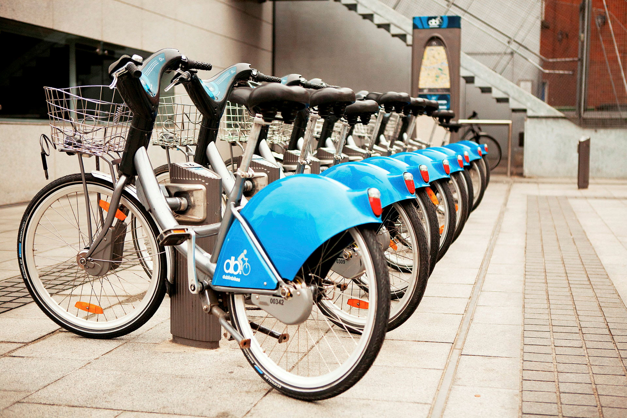 En rad parkerade blå hyrcyklar på rad vid en station. (AI-genererad text)
