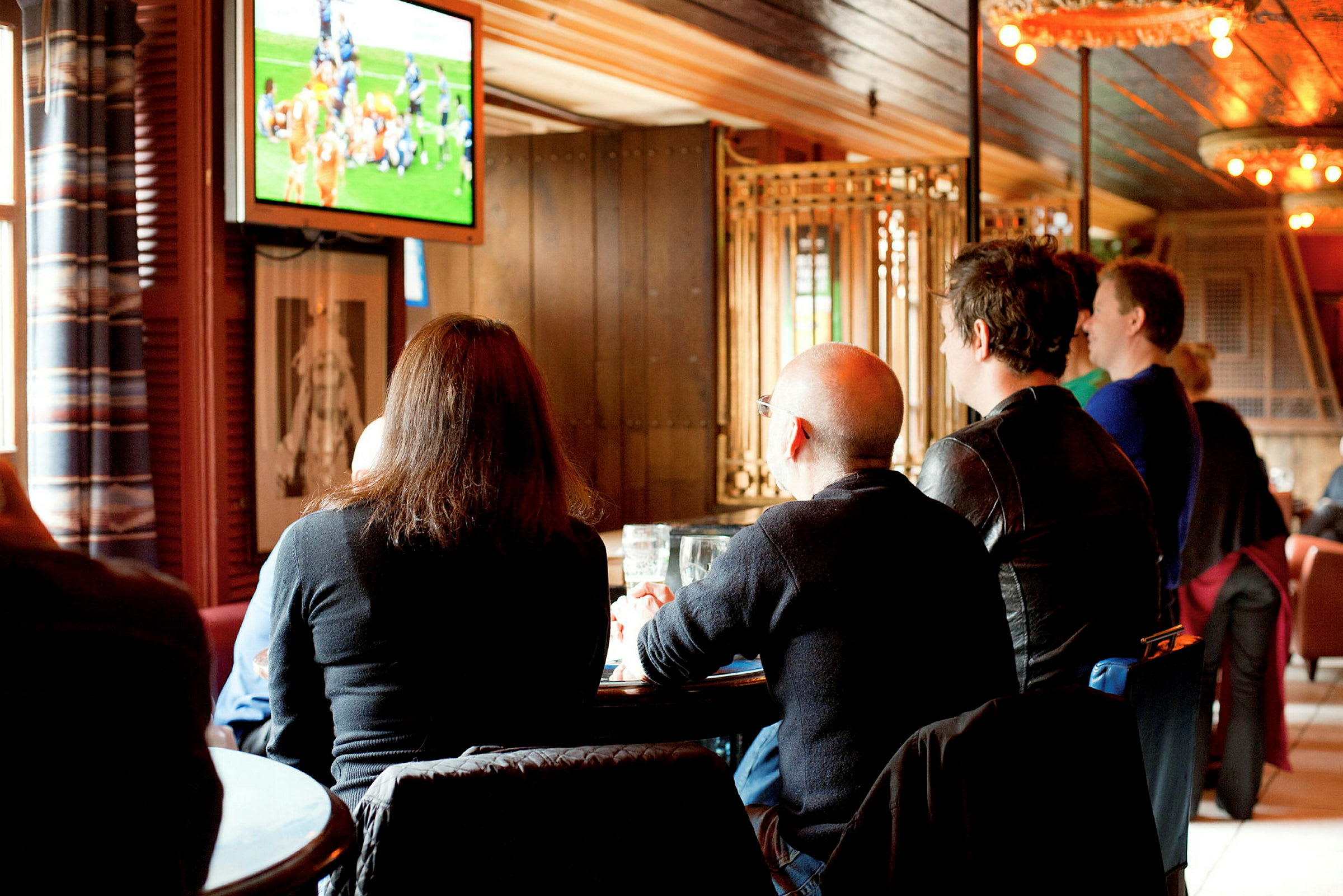 Personer sitter i en lokal och tittar på sport på en TV-skärm. (AI-genererad text)