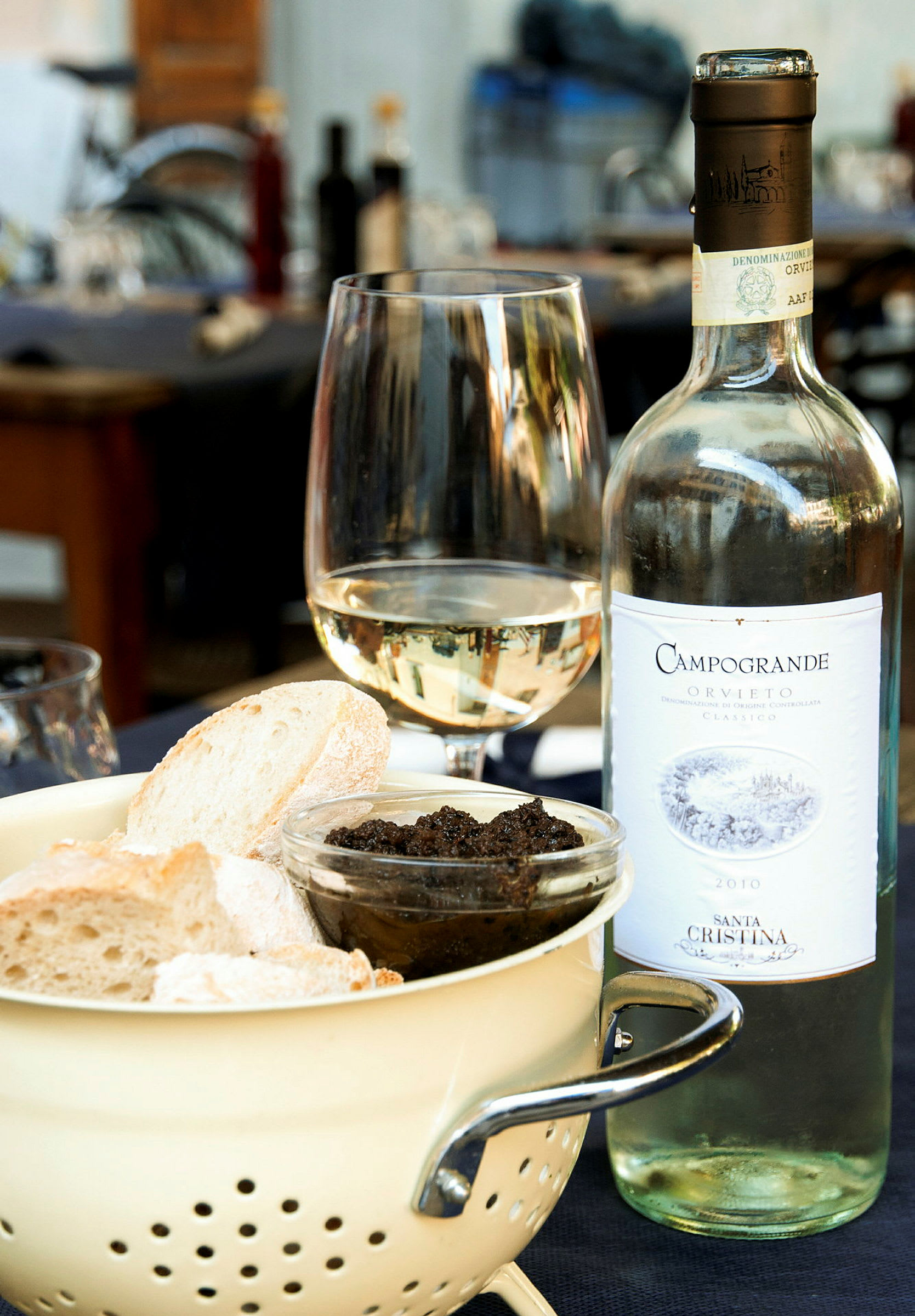 En flaska vitt vin, ett glas, en skål med bröd och en liten skål med mörk röra står på ett bord. (AI-genererad text)