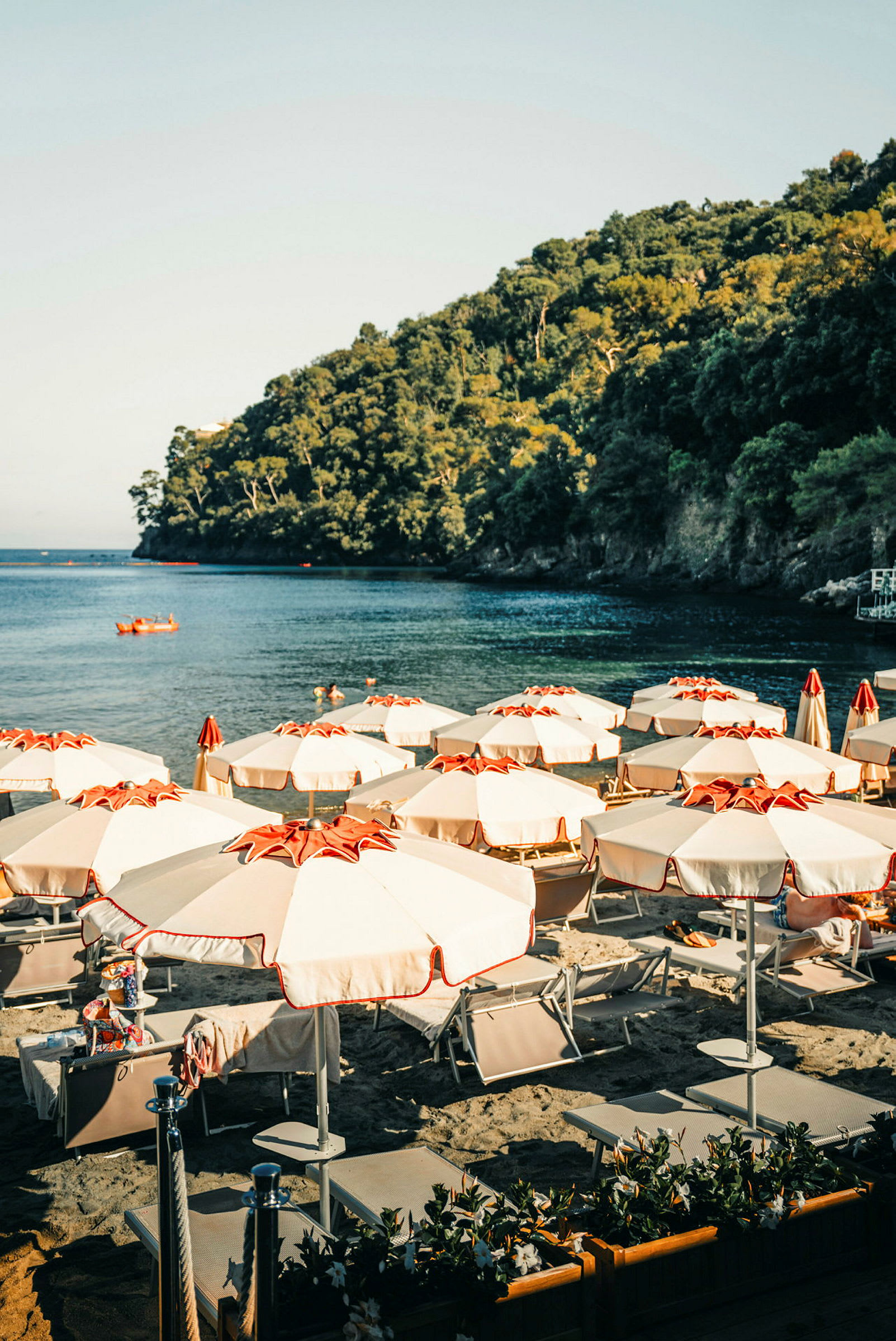 Solstolar och parasoller på en strand med utsikt mot havet och trädbeklädda klippor. (AI-genererad text)