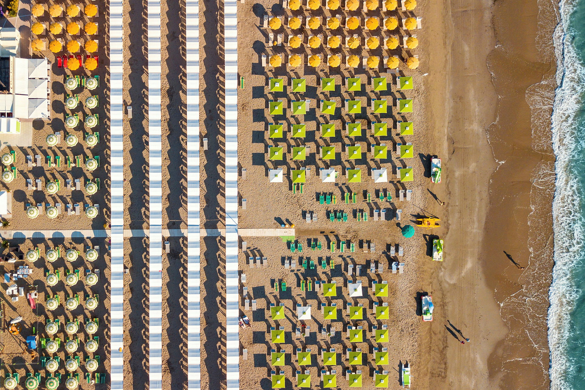 Flygbild av en solig strand med rader av solparasoller och solbäddar ordnade i mönster. (AI-genererad text)